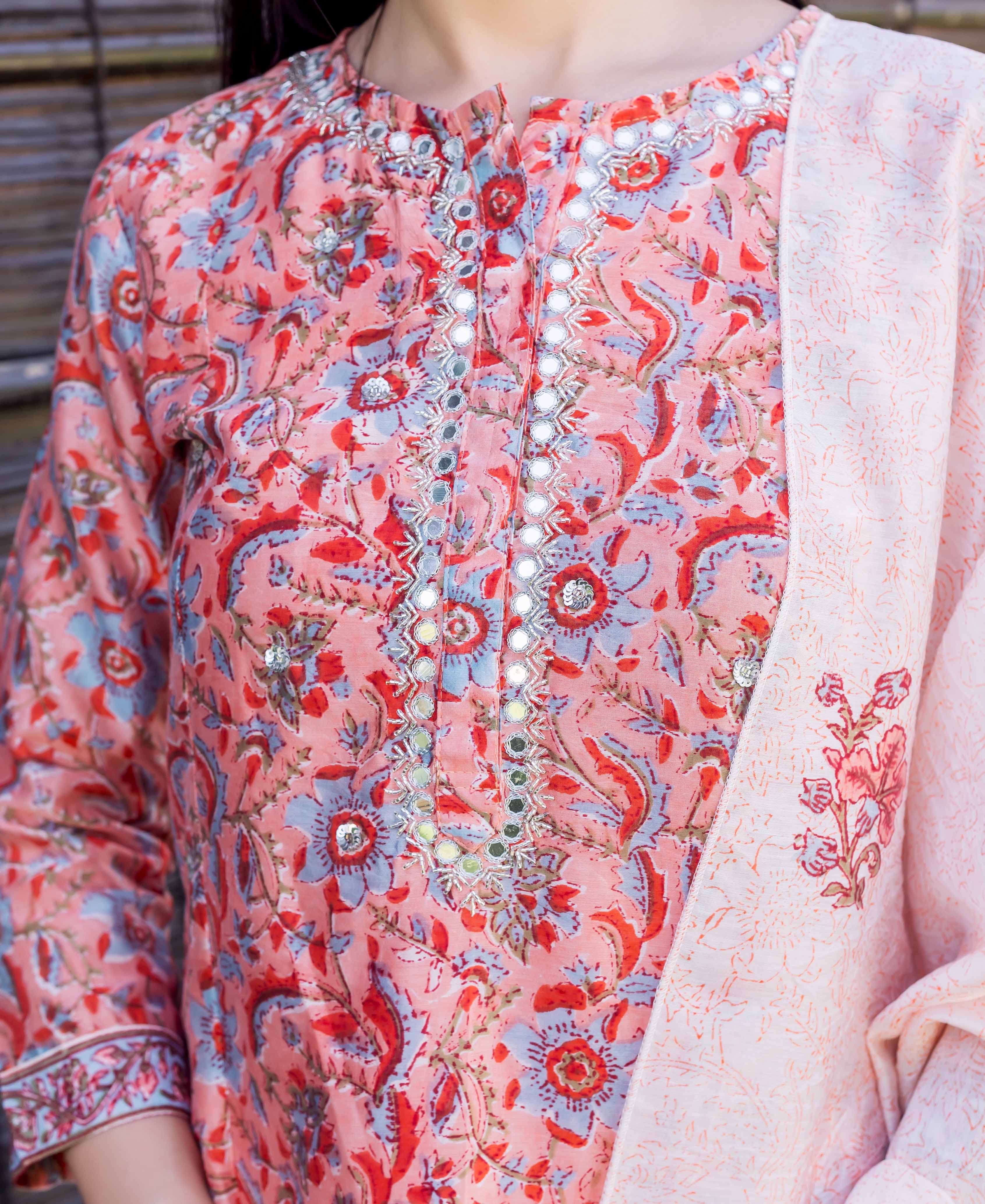 Model wearing peach block-printed kurta with red, blue floral print, mirror work, and dupatta.