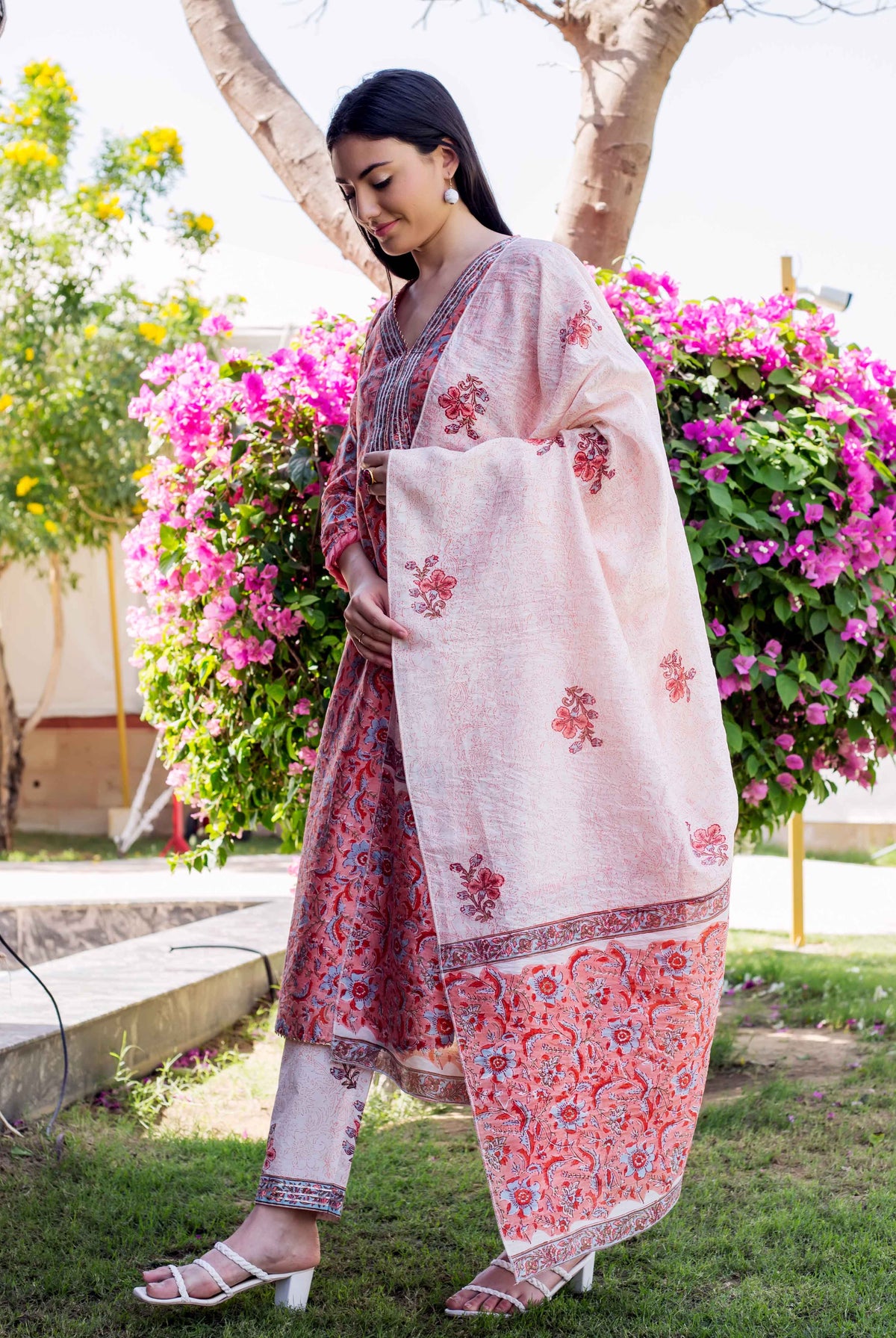 Woman in a red hand-block printed kurta set with dupatta, standing outdoors.