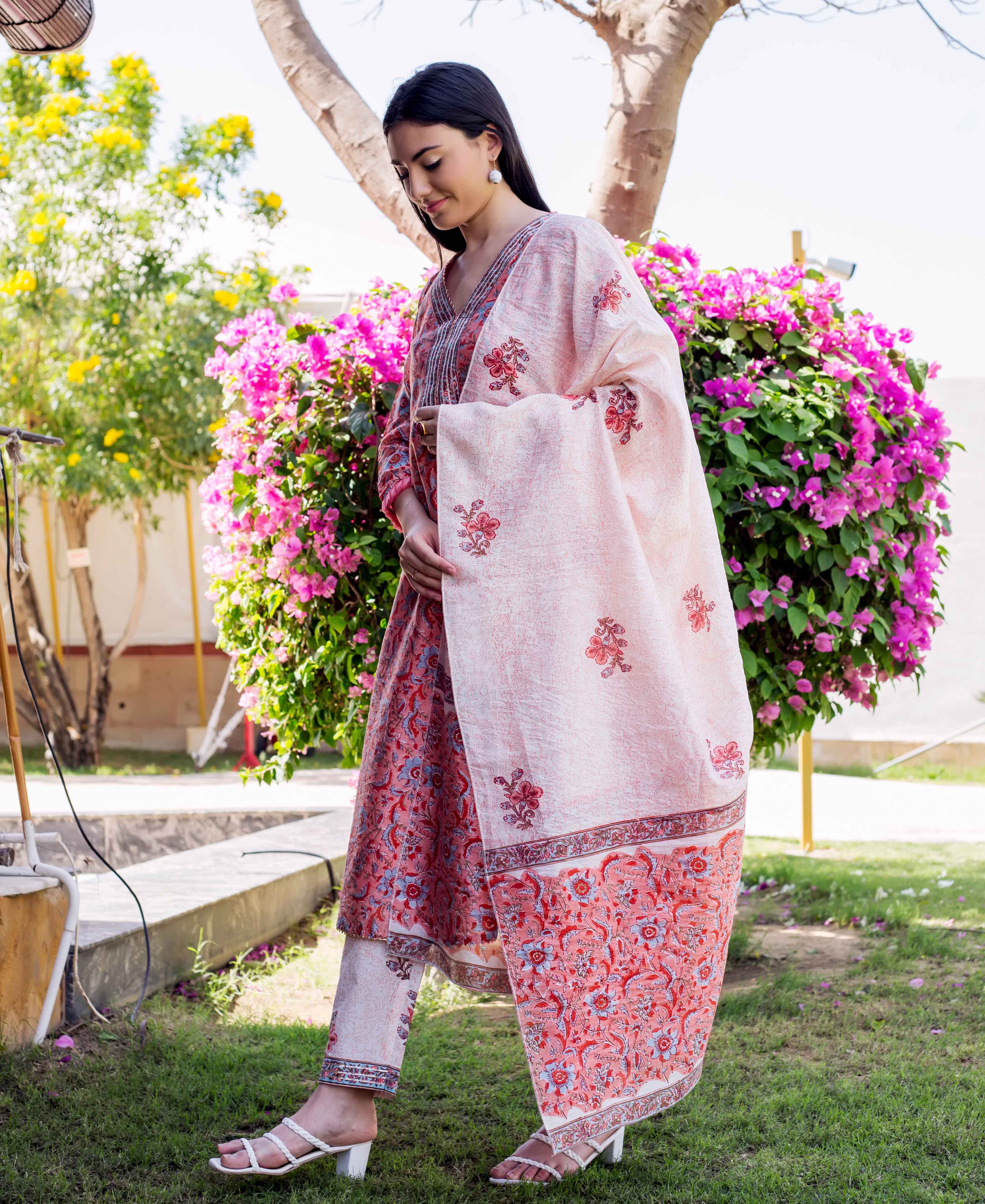 Woman in a red hand-block printed kurta set with dupatta, standing outdoors.