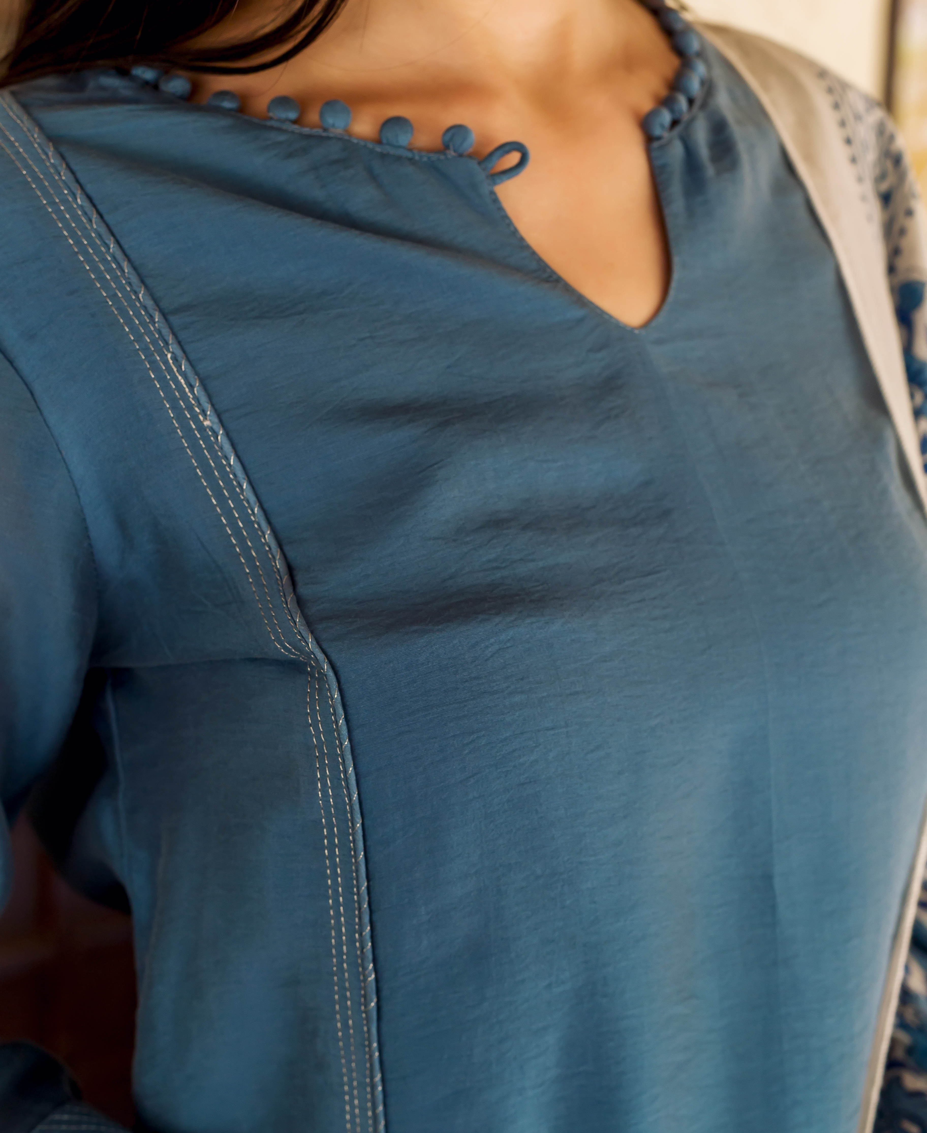 Model wears a Prussian blue embroidered kurta with a V-neckline and decorative fabric buttons.