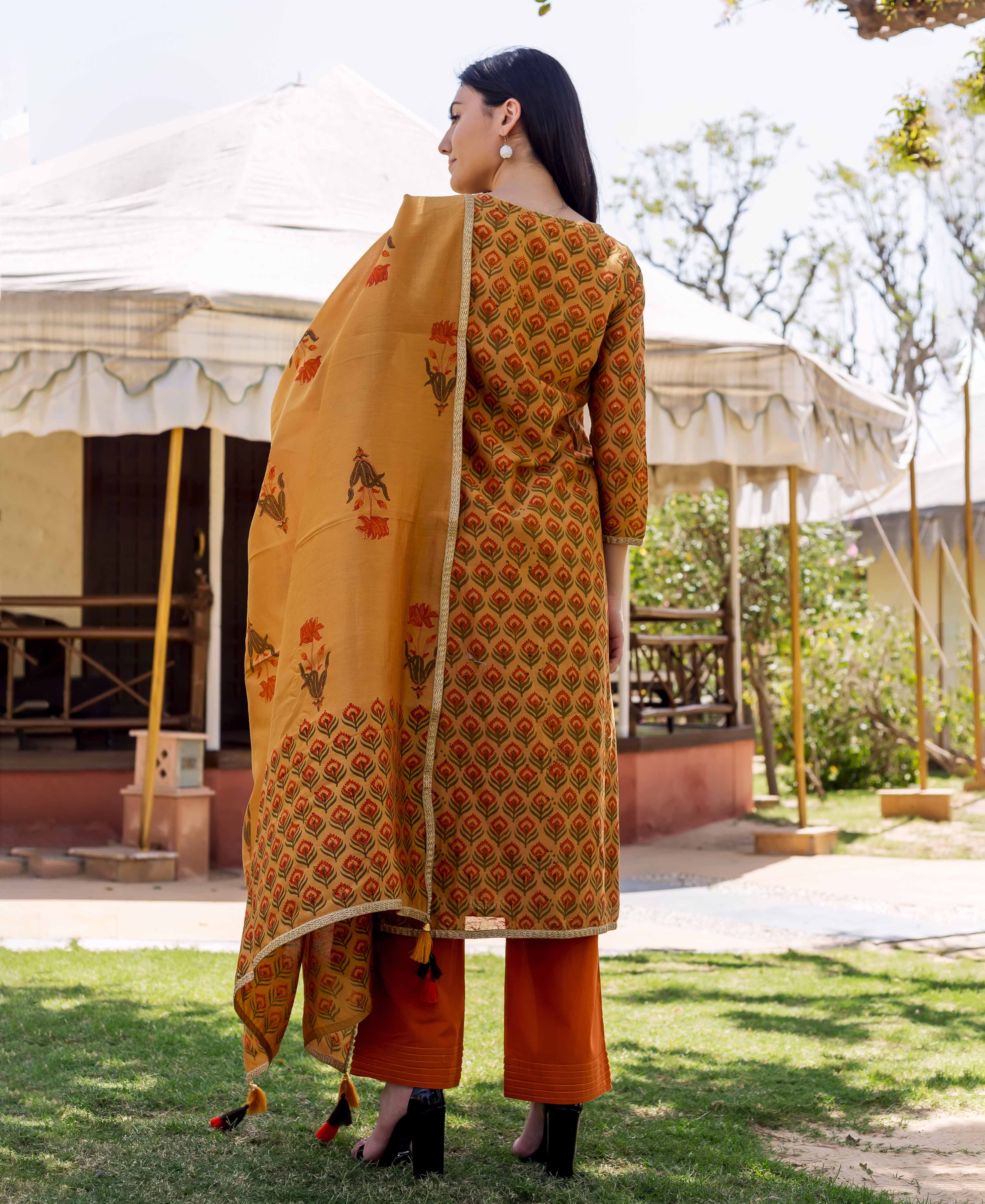 Rear view of model wearing mustard block-printed kurta, orange pants, and floral dupatta.