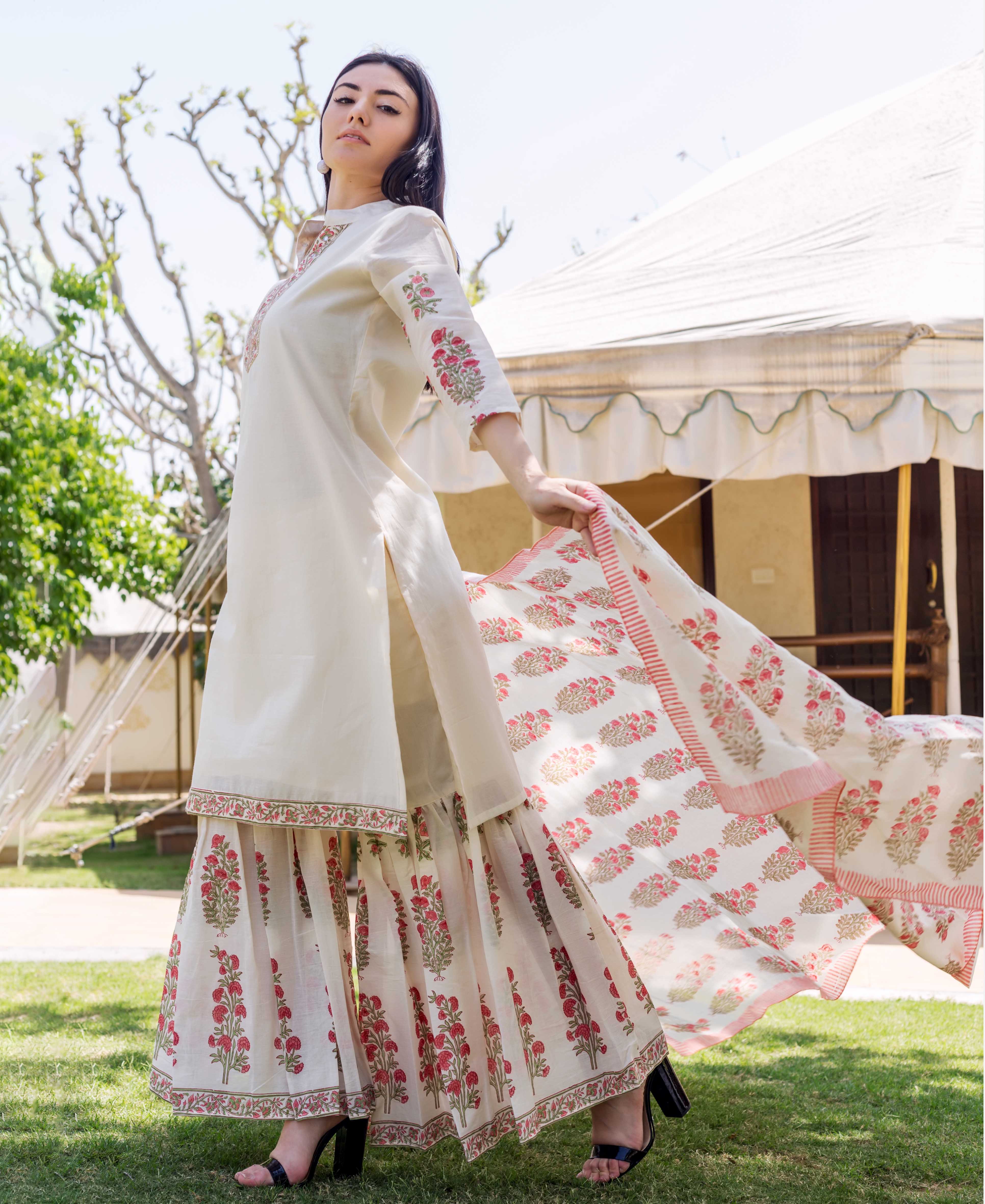 A woman in a long, white dress with pink floral patterns and a matching dupatta.
