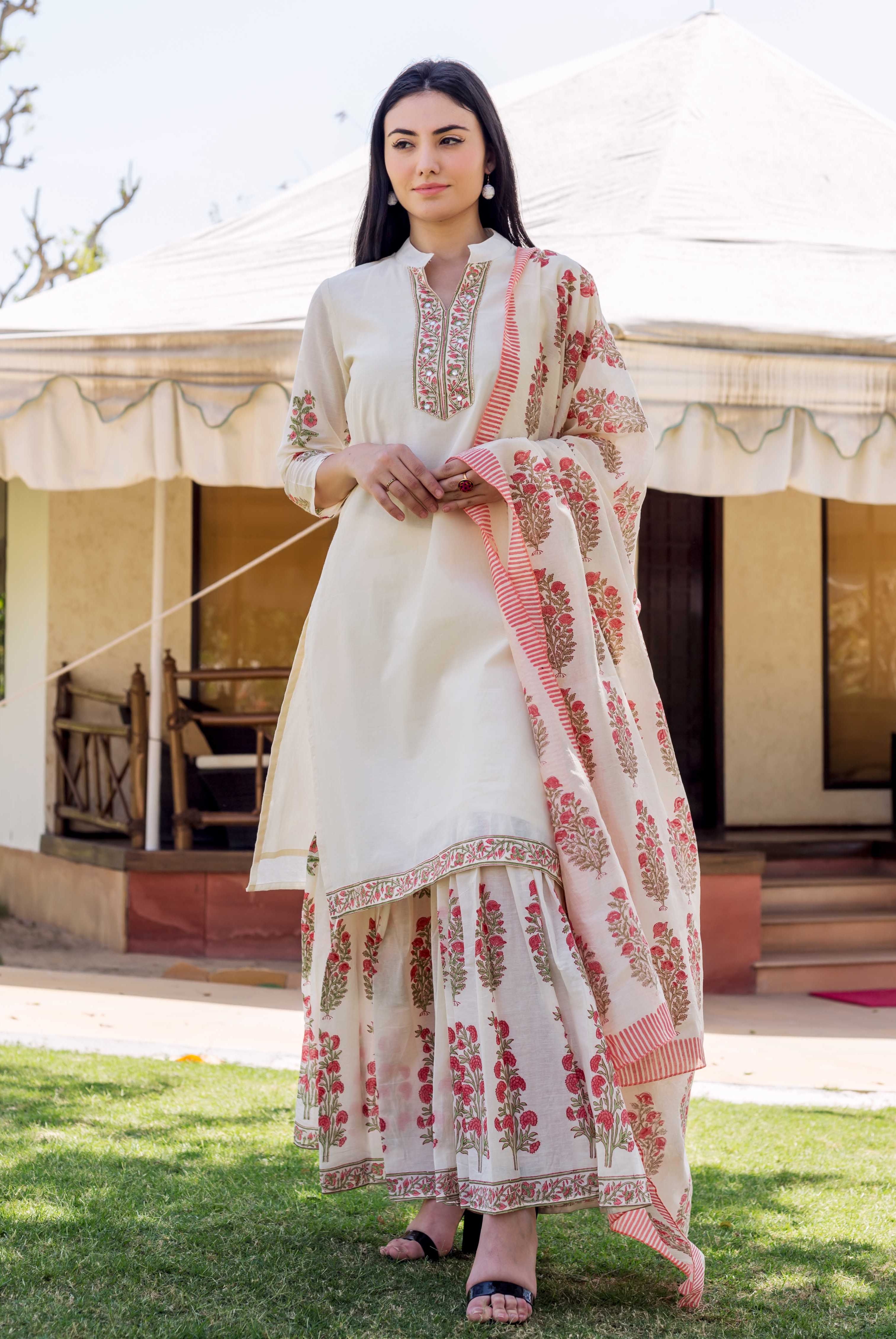 A woman in a long, white kurta with red and green floral patterns.
