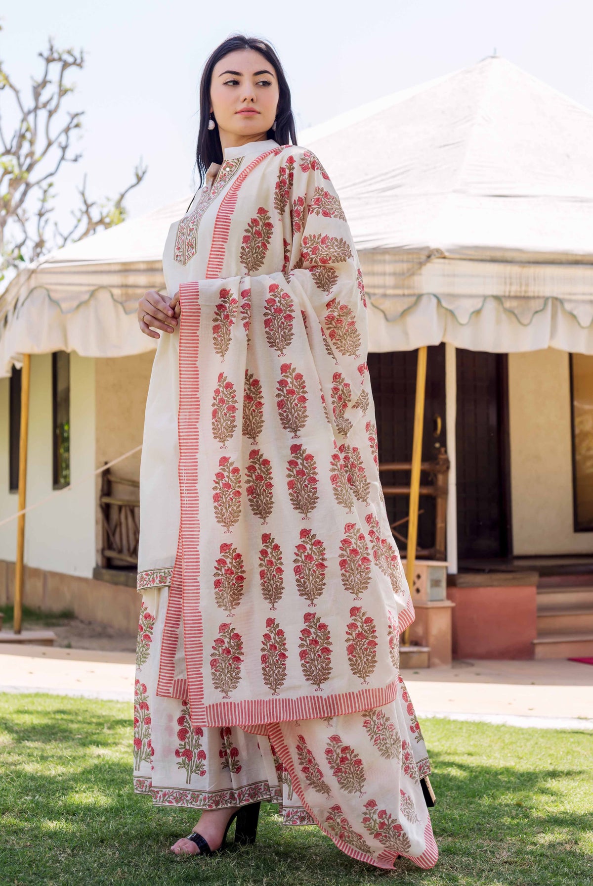 A woman in a long, white kurta with red and gold floral patterns.