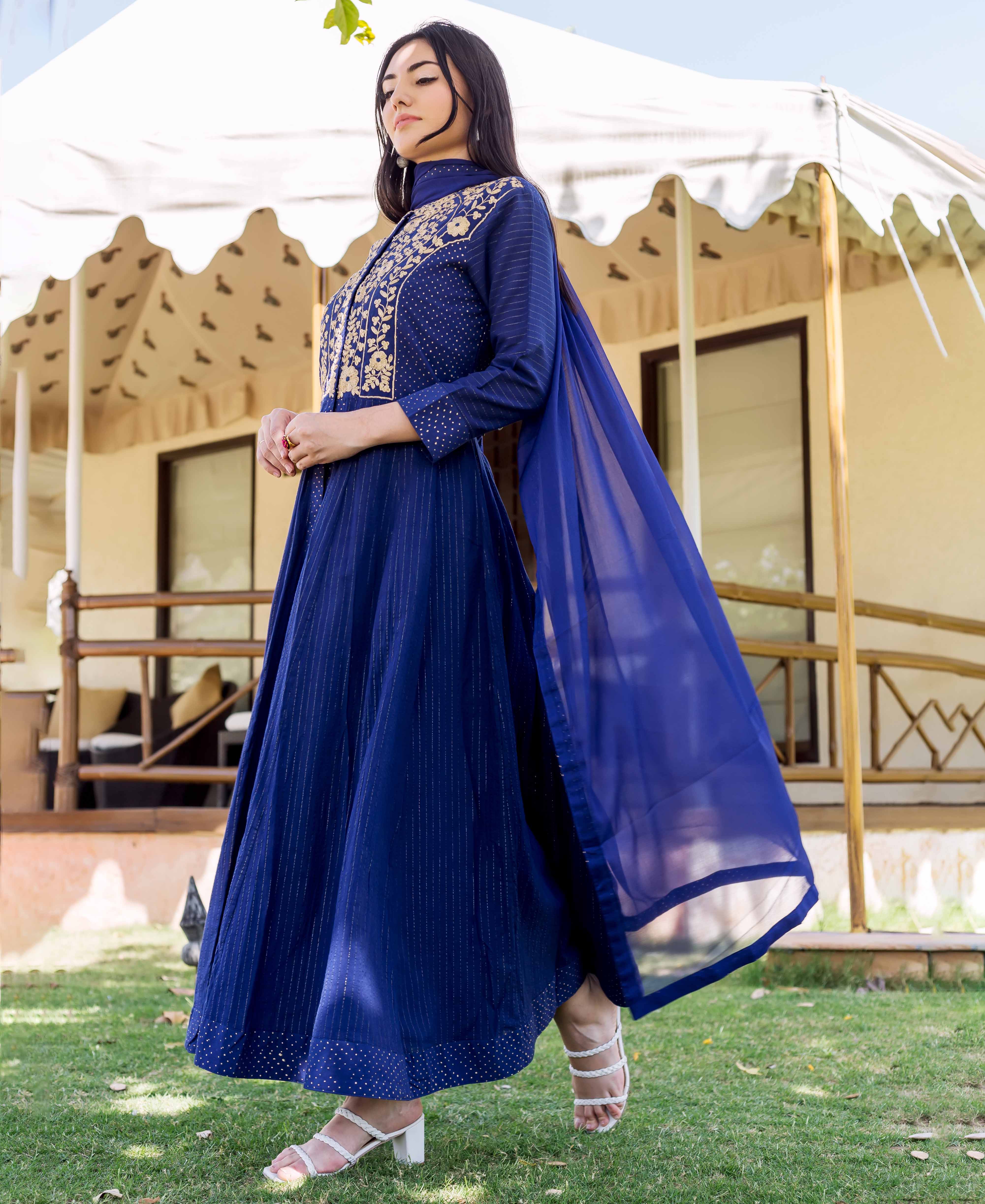 A woman in a royal blue dress with gold embroidery and a sheer blue scarf.