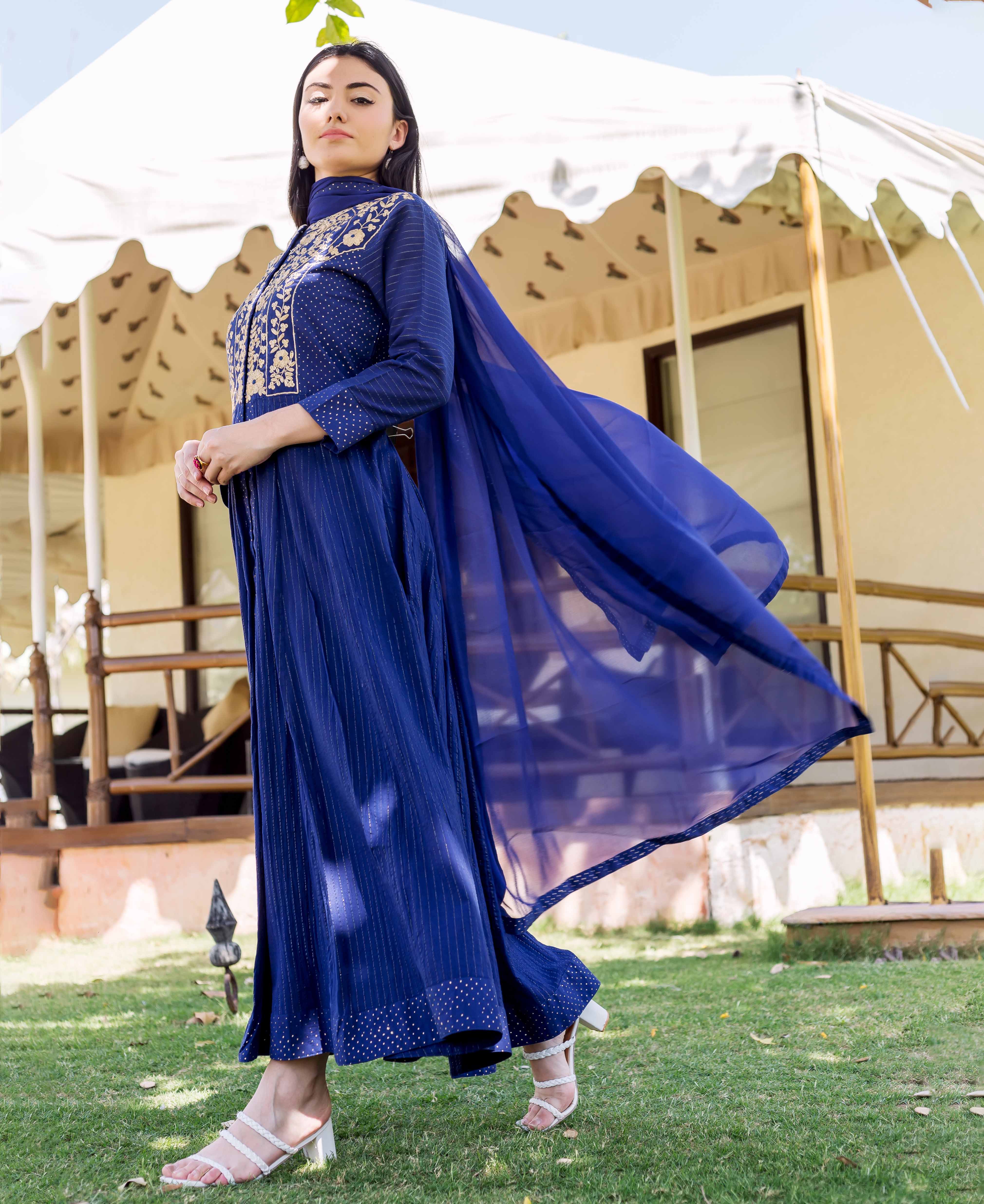 Model wears royal blue long dress with gold floral embroidery, block prints, and flowing dupatta.