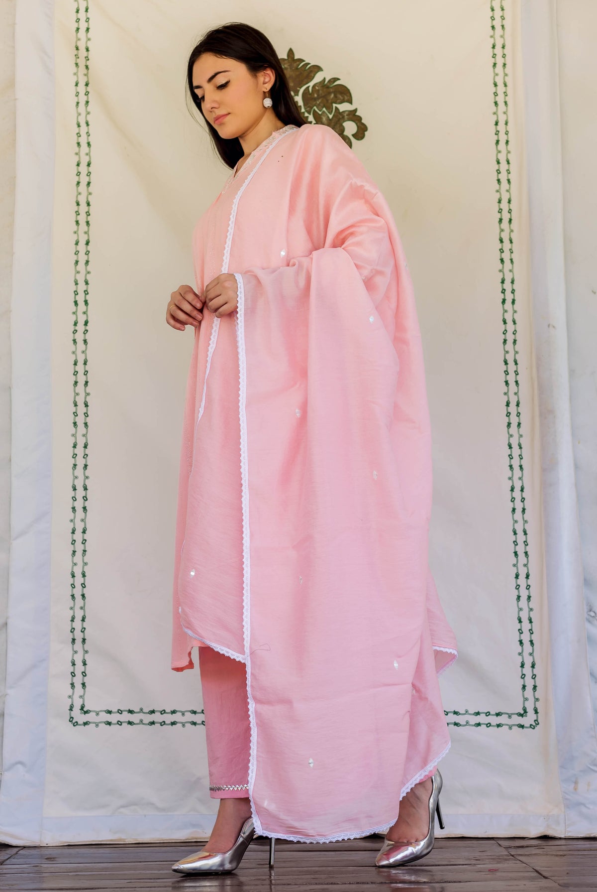 Side view of model in a light pink embroidered kurta set with white lace trim.