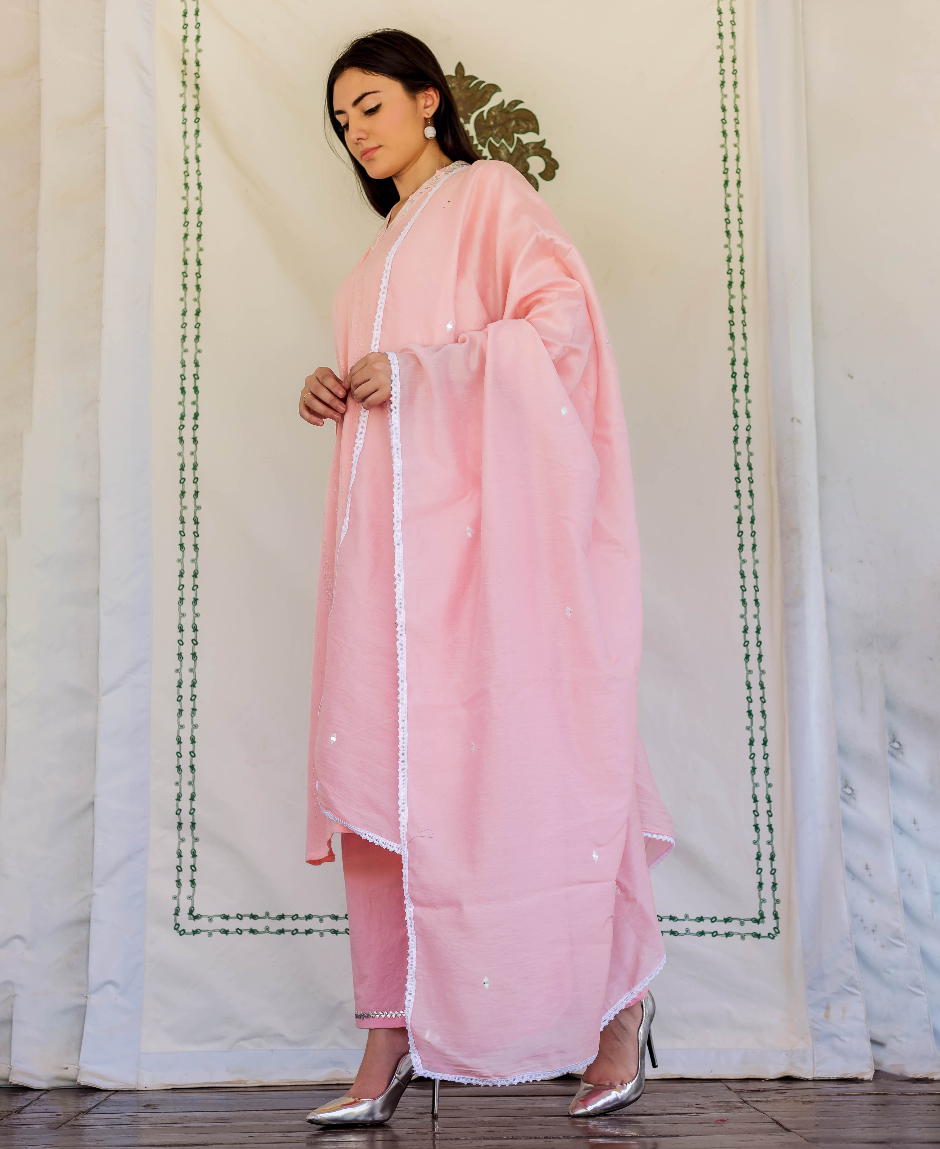 Side view of model in a light pink embroidered kurta set with white lace trim.
