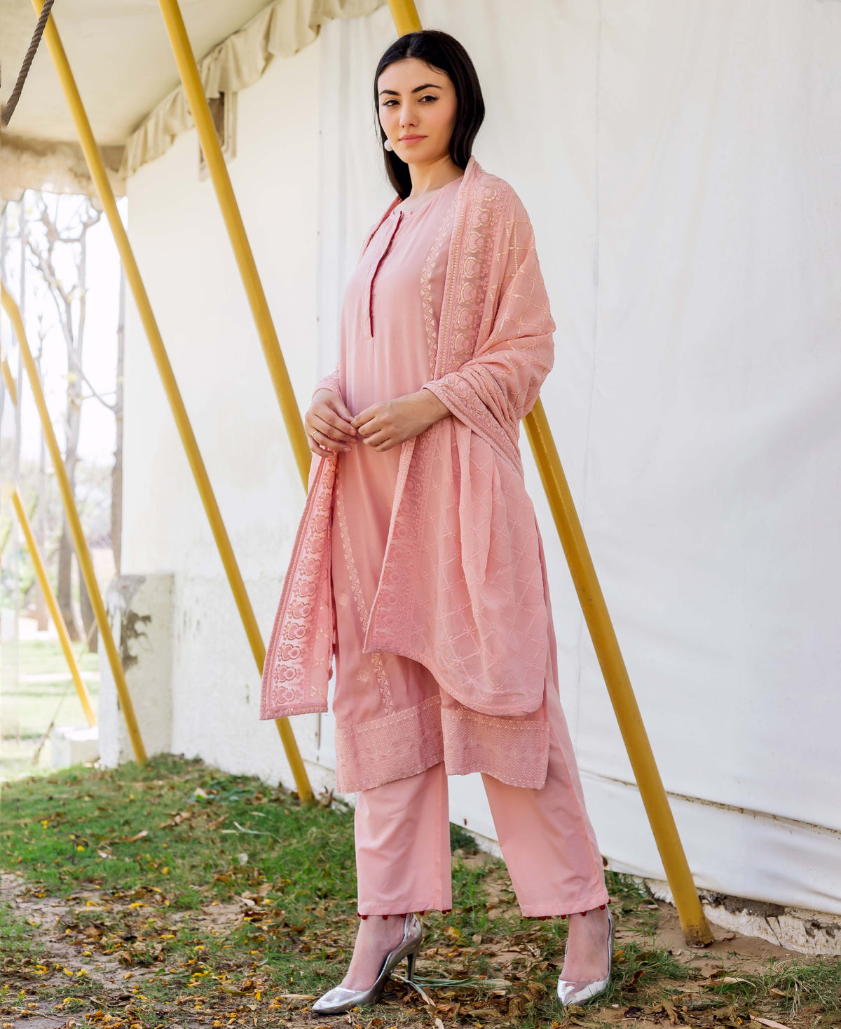 Woman in dusty pink embroidered kurta and pants, standing outdoors with white fabric background.