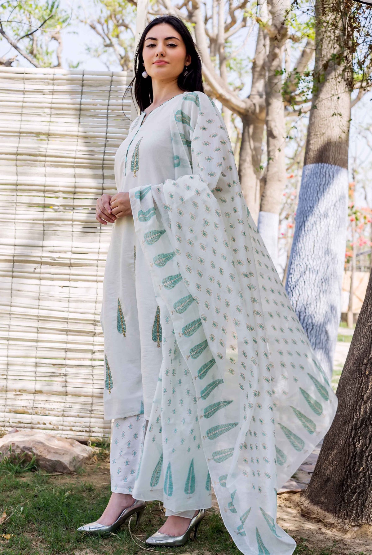 A woman in a white kurta with green leaf prints and embroidery, standing outdoors.