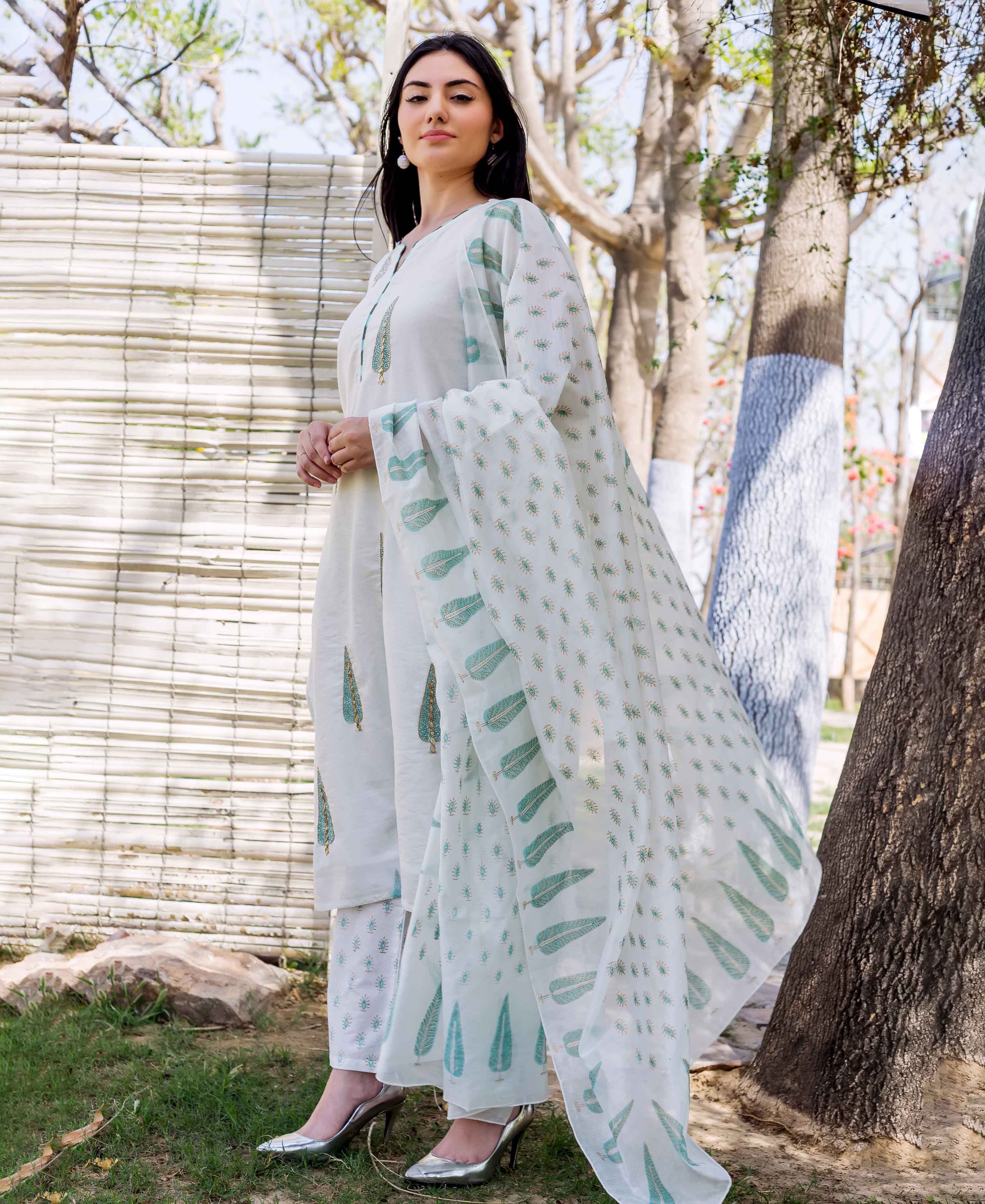 A woman in a white kurta with green leaf prints and embroidery, standing outdoors.