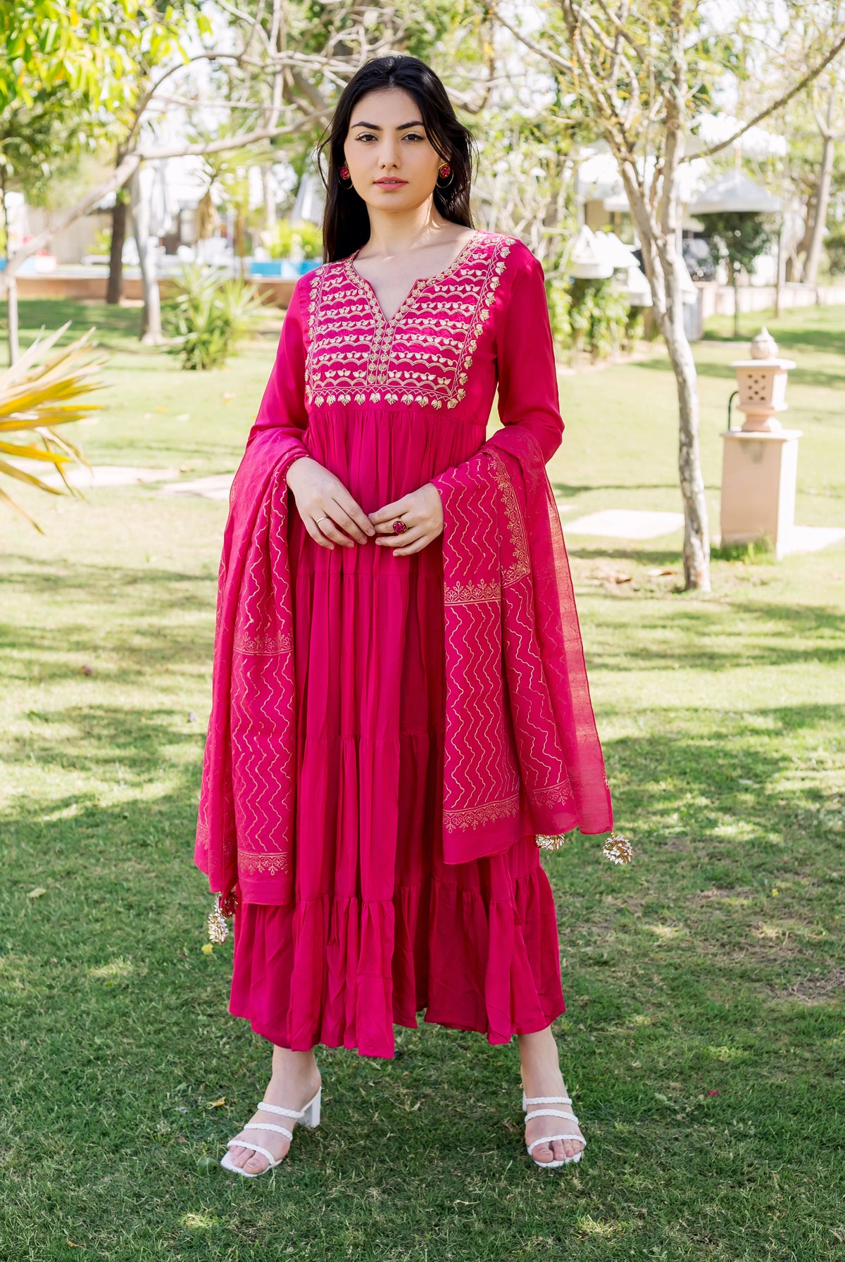 Raspberry red tiered dress with embroidered bodice and gold detailing, on a female model outdoors.