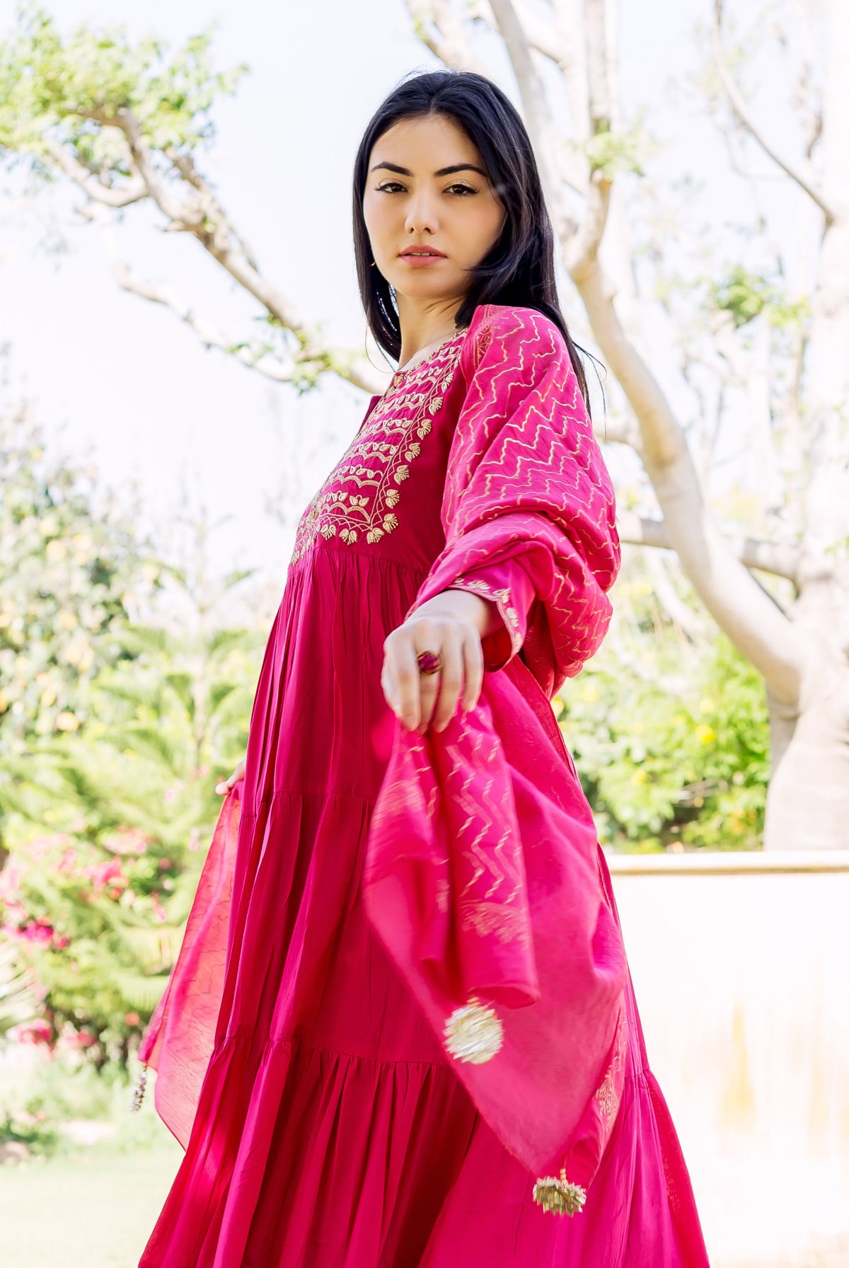 Woman in raspberry red tiered ethnic dress with gold embroidery and zigzag print.