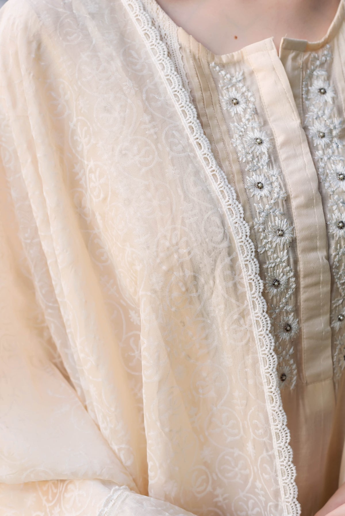 Close-up of a cream ethnic kurta with embroidered pintucks, delicate lace, and subtle block print.