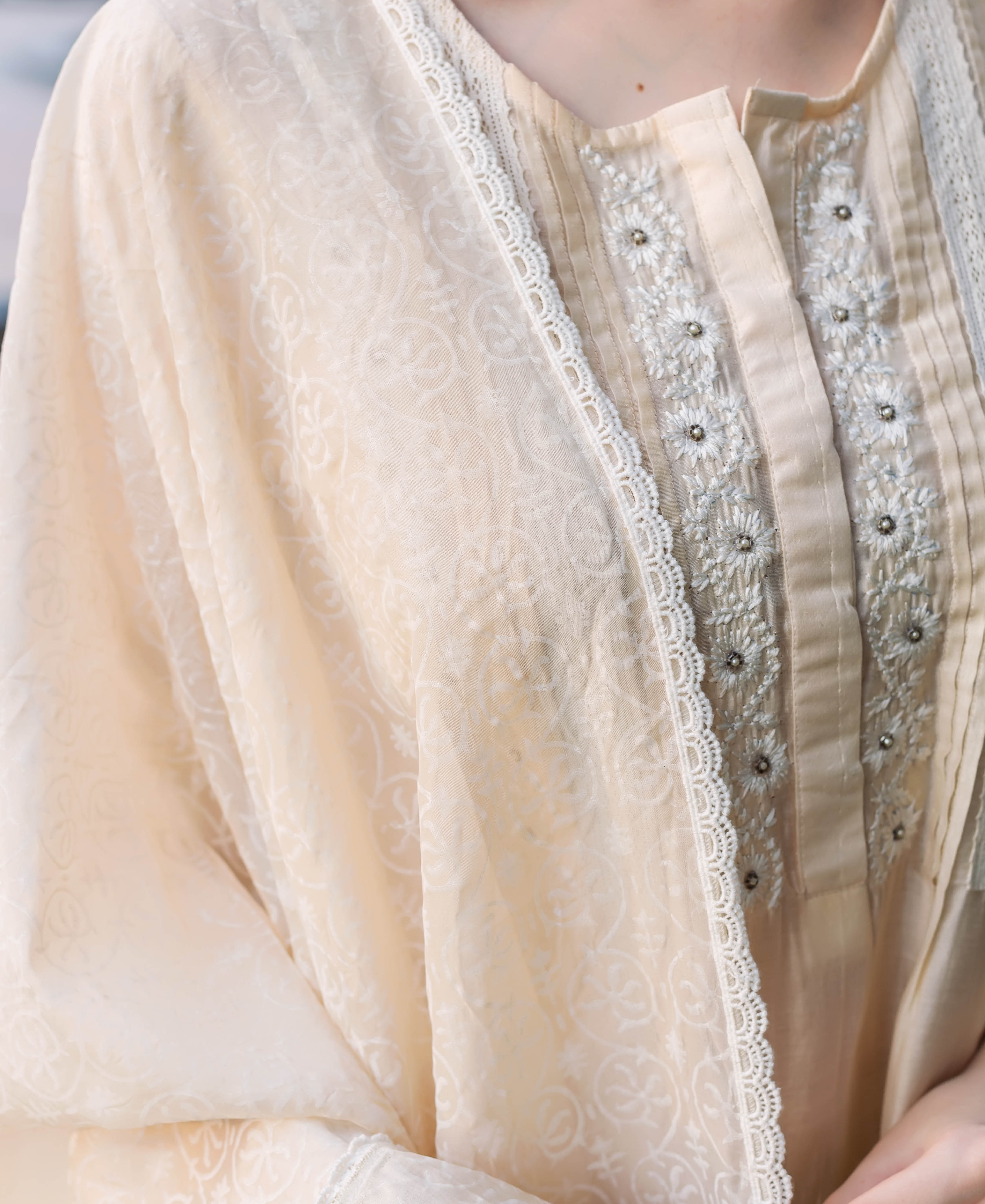 Close-up of a cream ethnic kurta with embroidered pintucks, delicate lace, and subtle block print.
