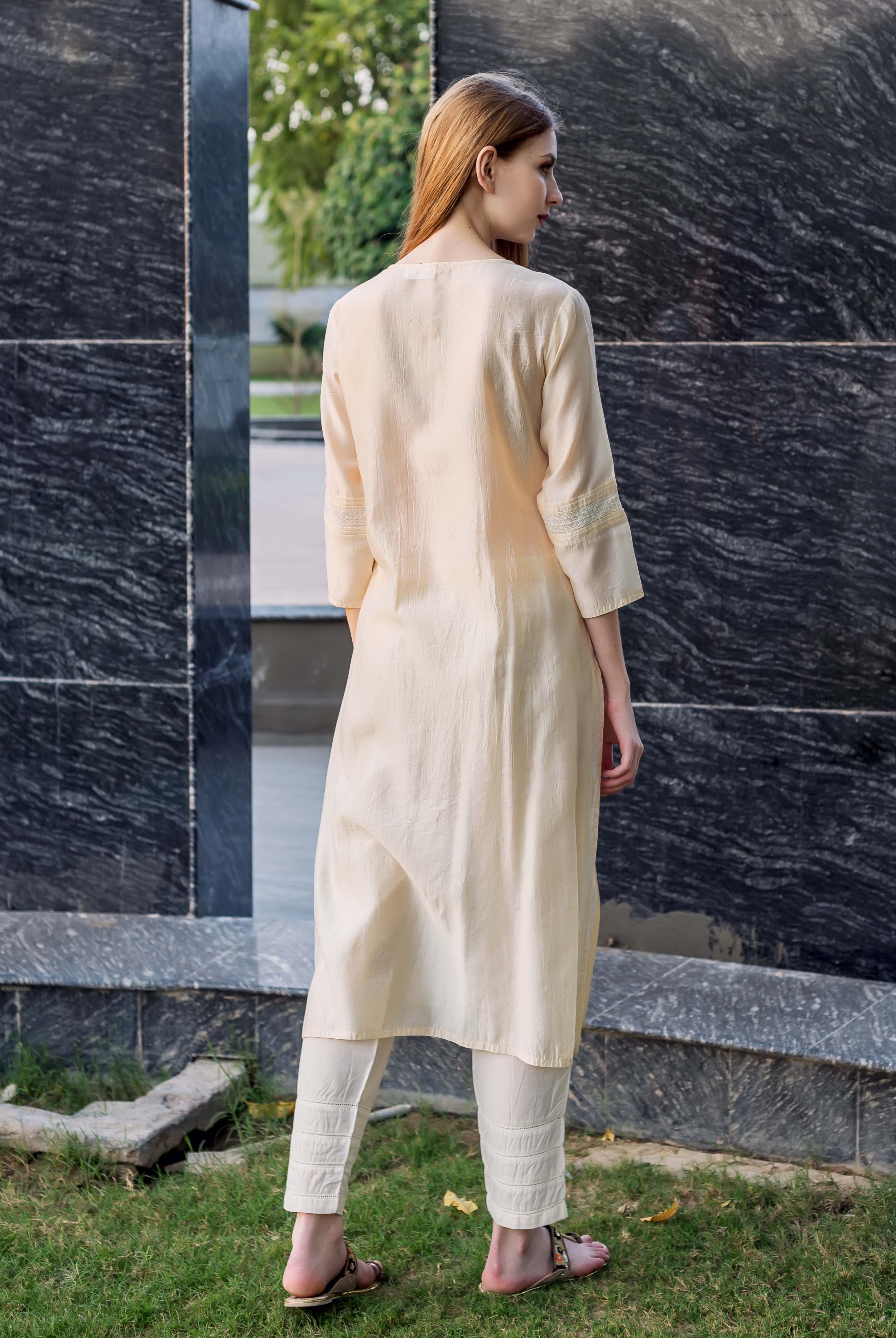 Rear view of model in an off-white straight kurta and matching trousers with pintucks.