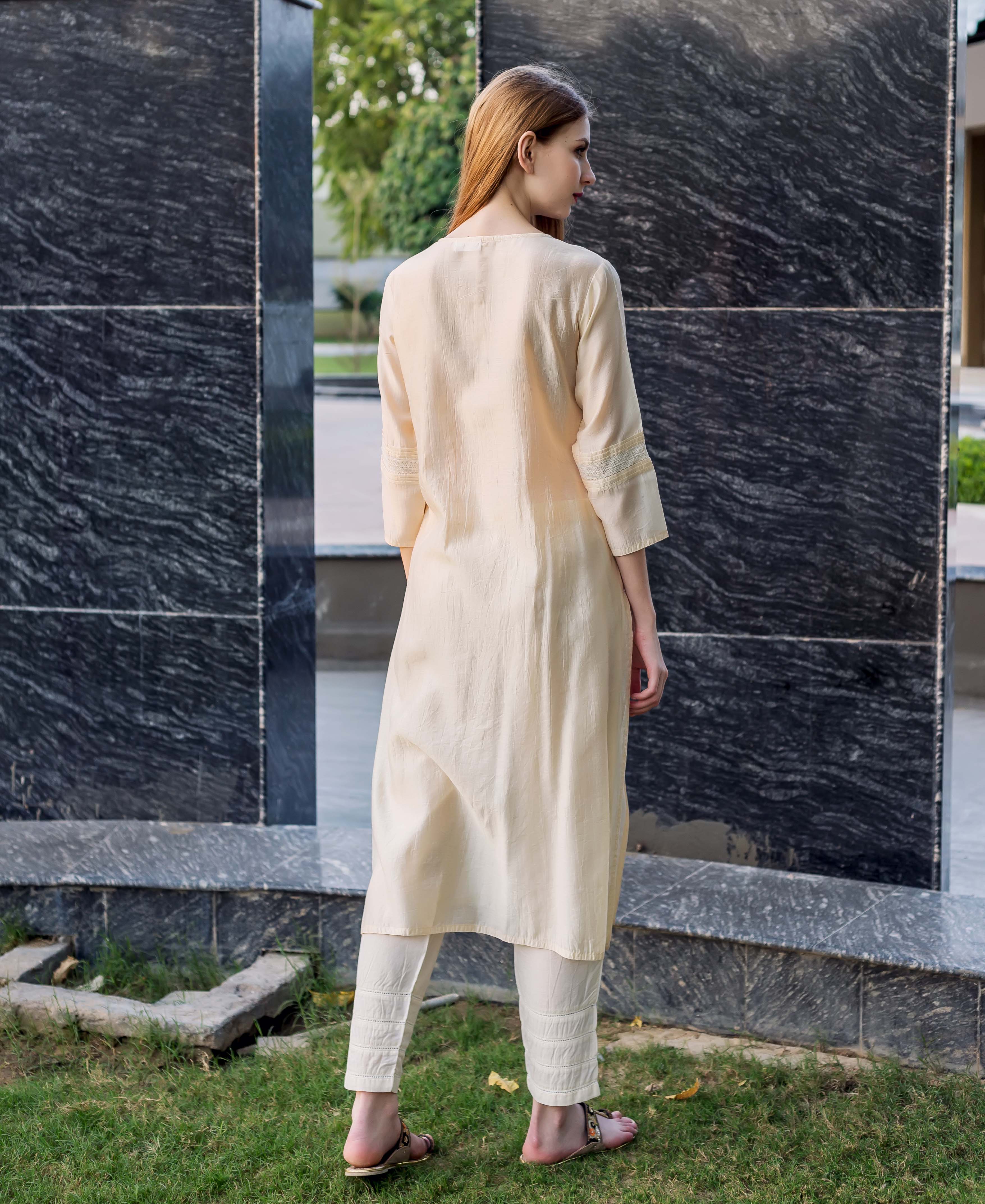 Rear view of model in an off-white straight kurta and matching trousers with pintucks.
