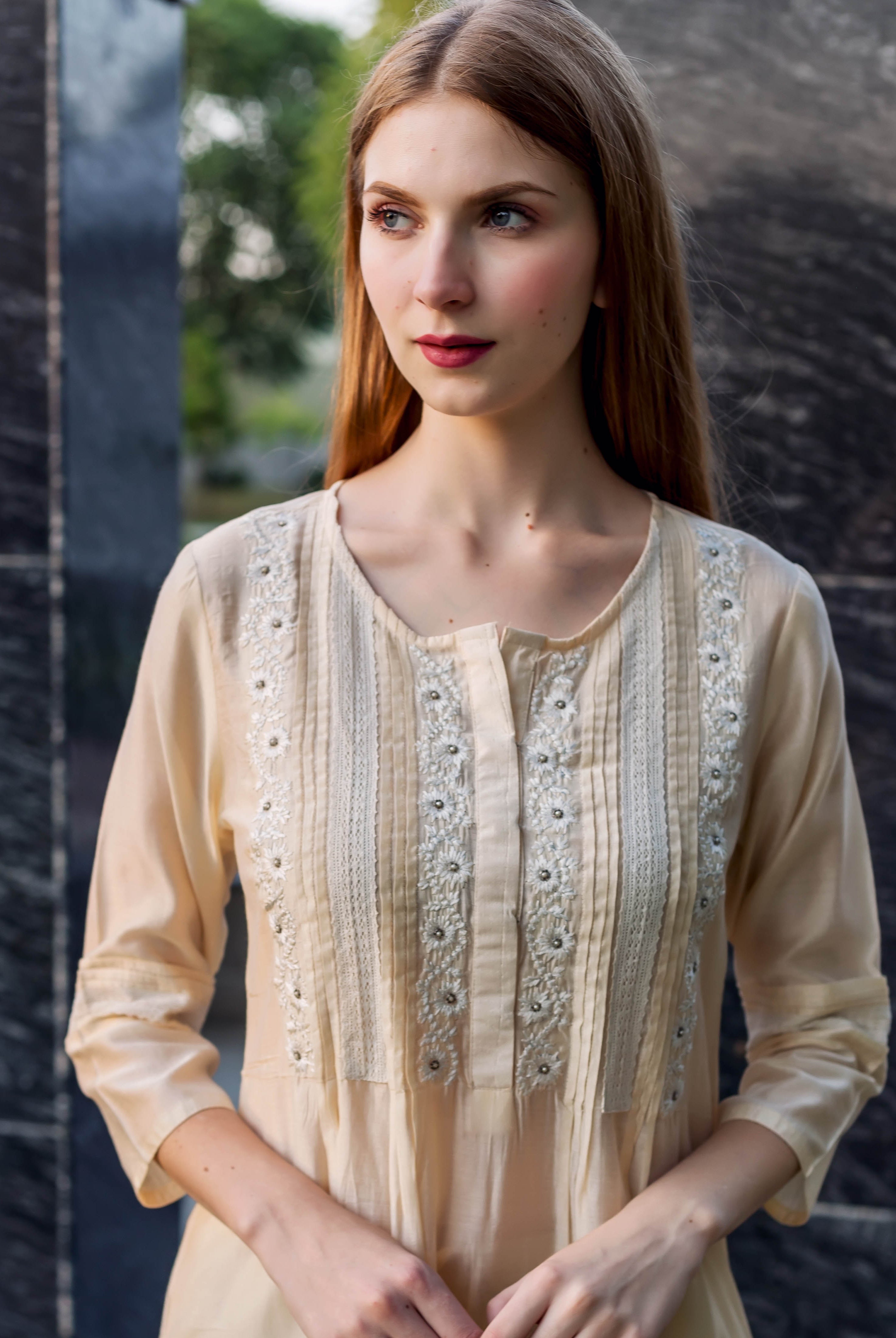 Young woman models an off-white embroidered kurta with pintuck and lace details.