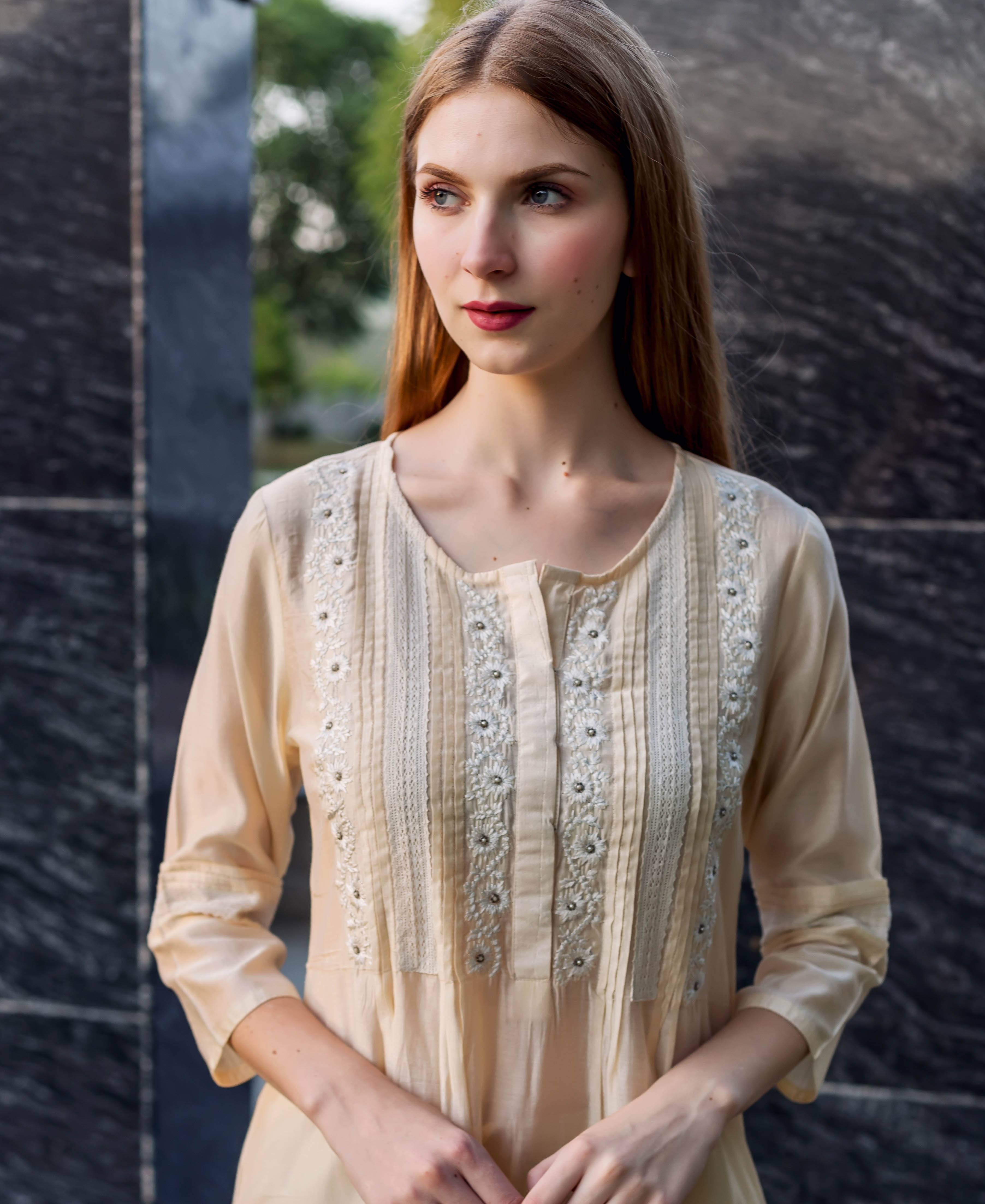 Young woman models an off-white embroidered kurta with pintuck and lace details.