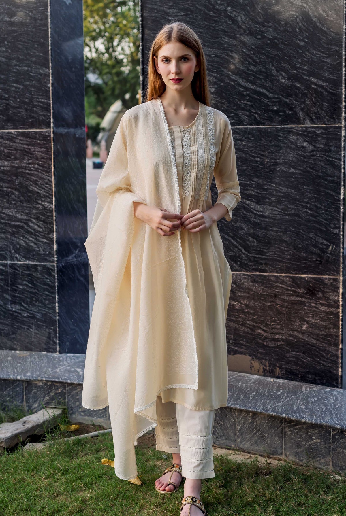 Model wearing off-white embroidered kurta set with pintuck detailing, lace trim, and matching dupatta.