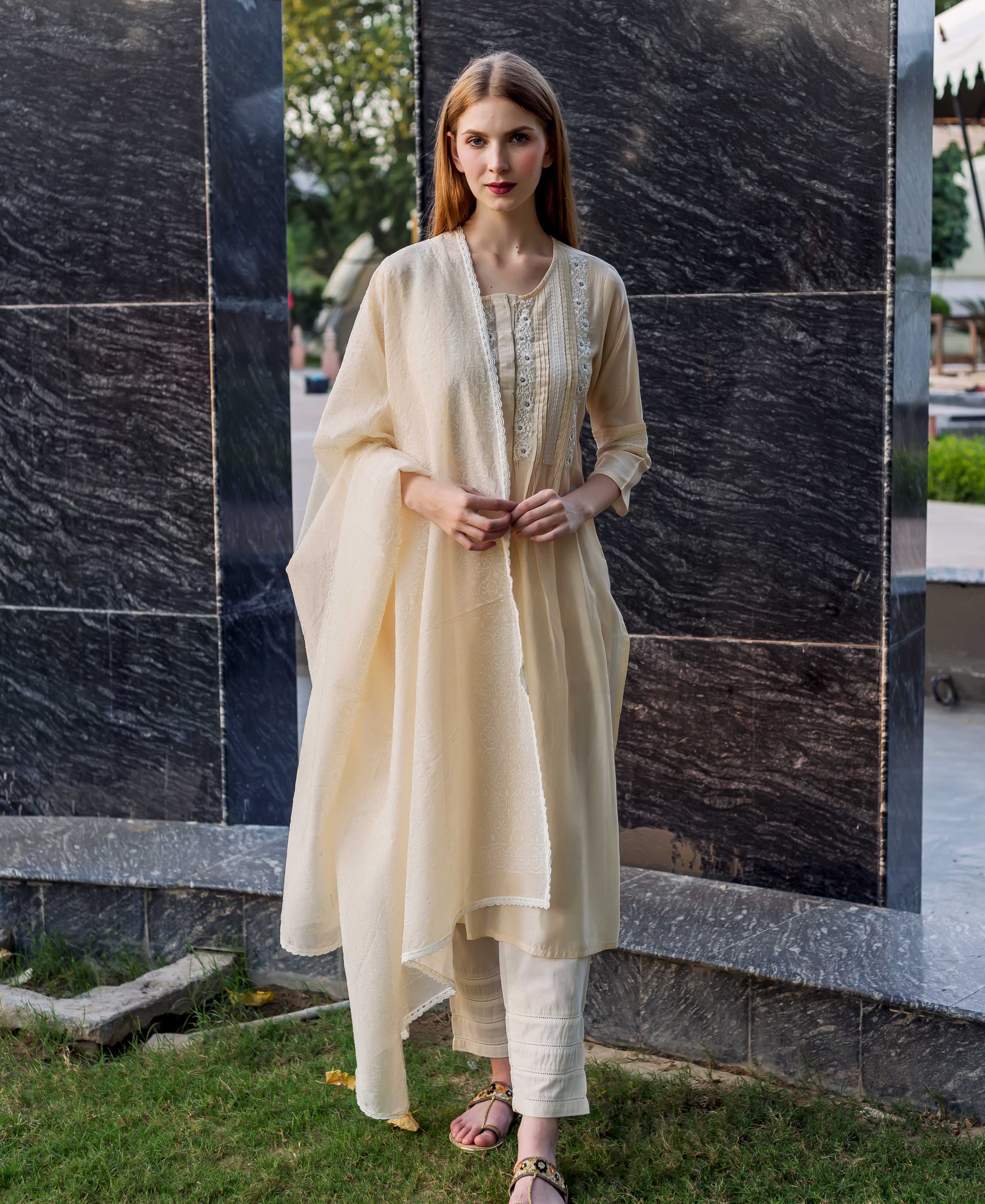 Model wearing off-white embroidered kurta set with pintuck detailing, lace trim, and matching dupatta.
