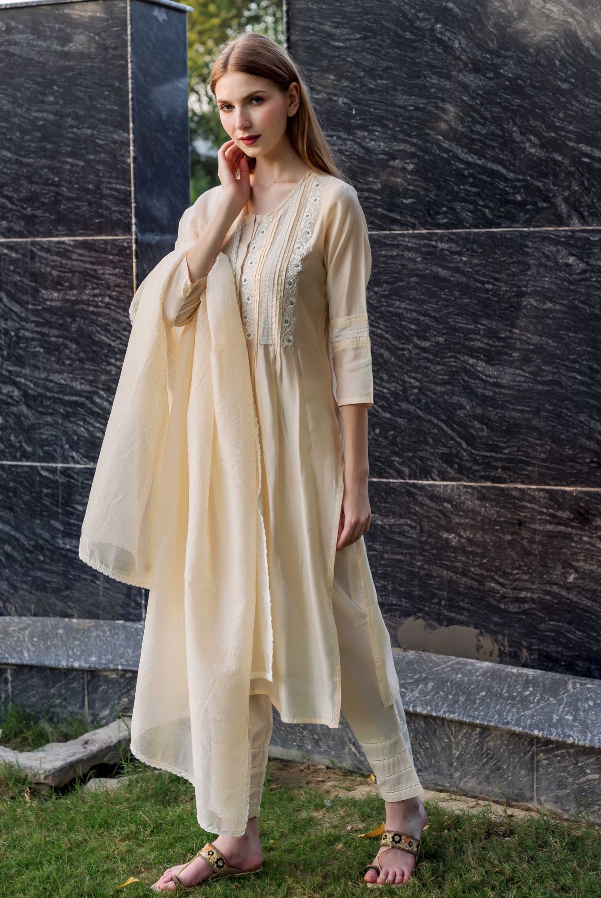 Full-length shot of a model wearing an off-white embroidered kurta set with pintuck and lace details.