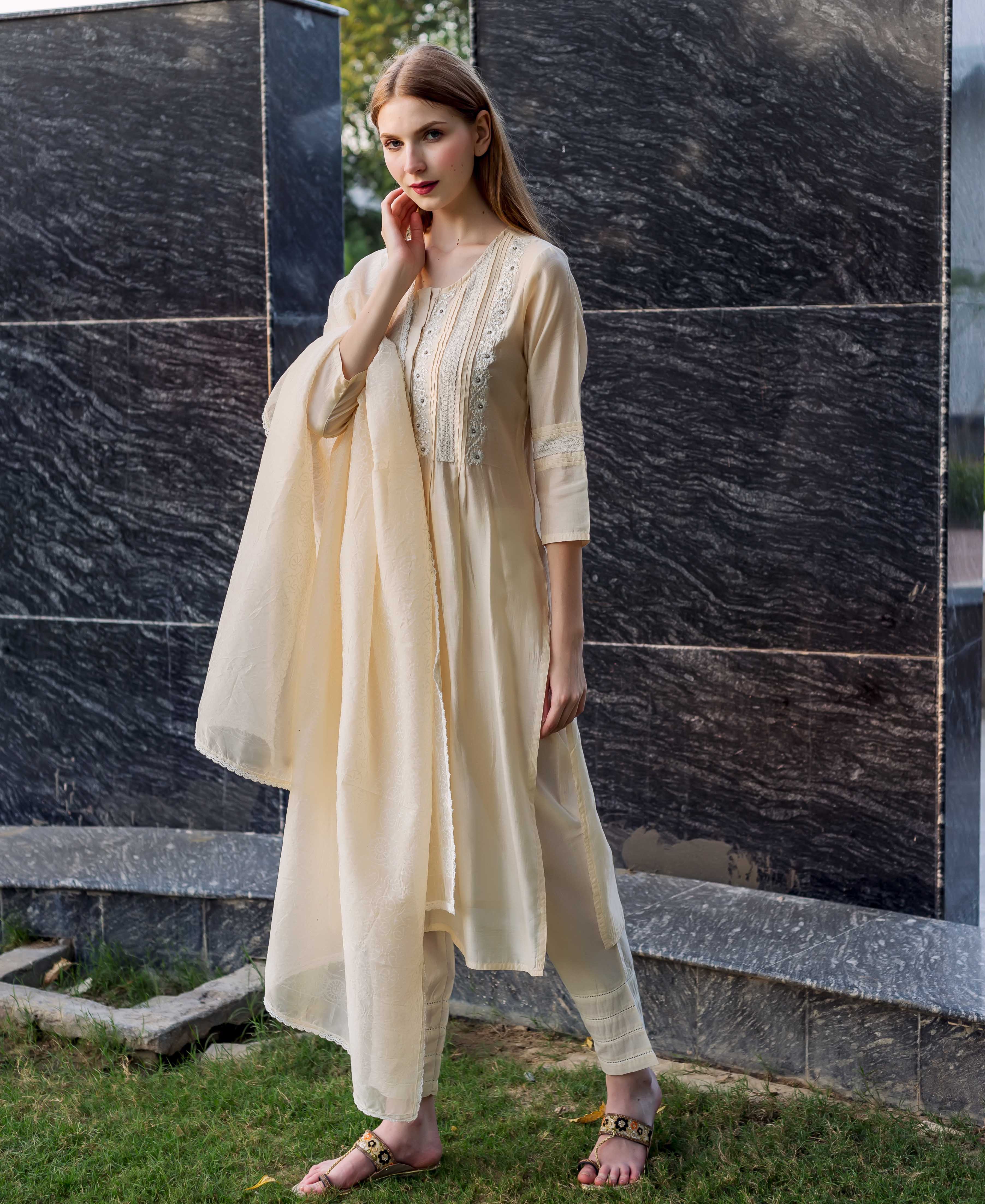 Full-length shot of a model wearing an off-white embroidered kurta set with pintuck and lace details.