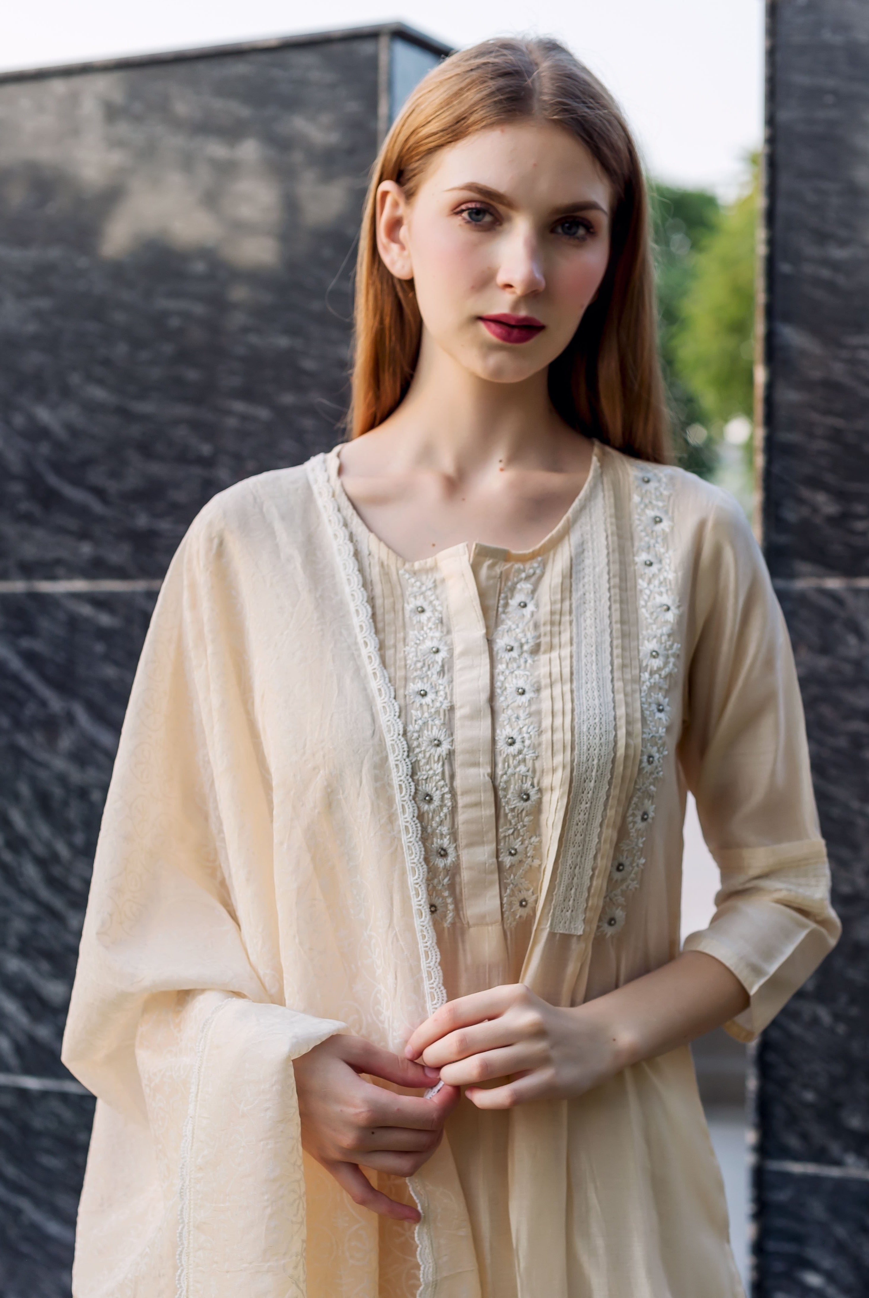 Front view of model wearing an off-white embroidered kurta with pintuck and lace details.