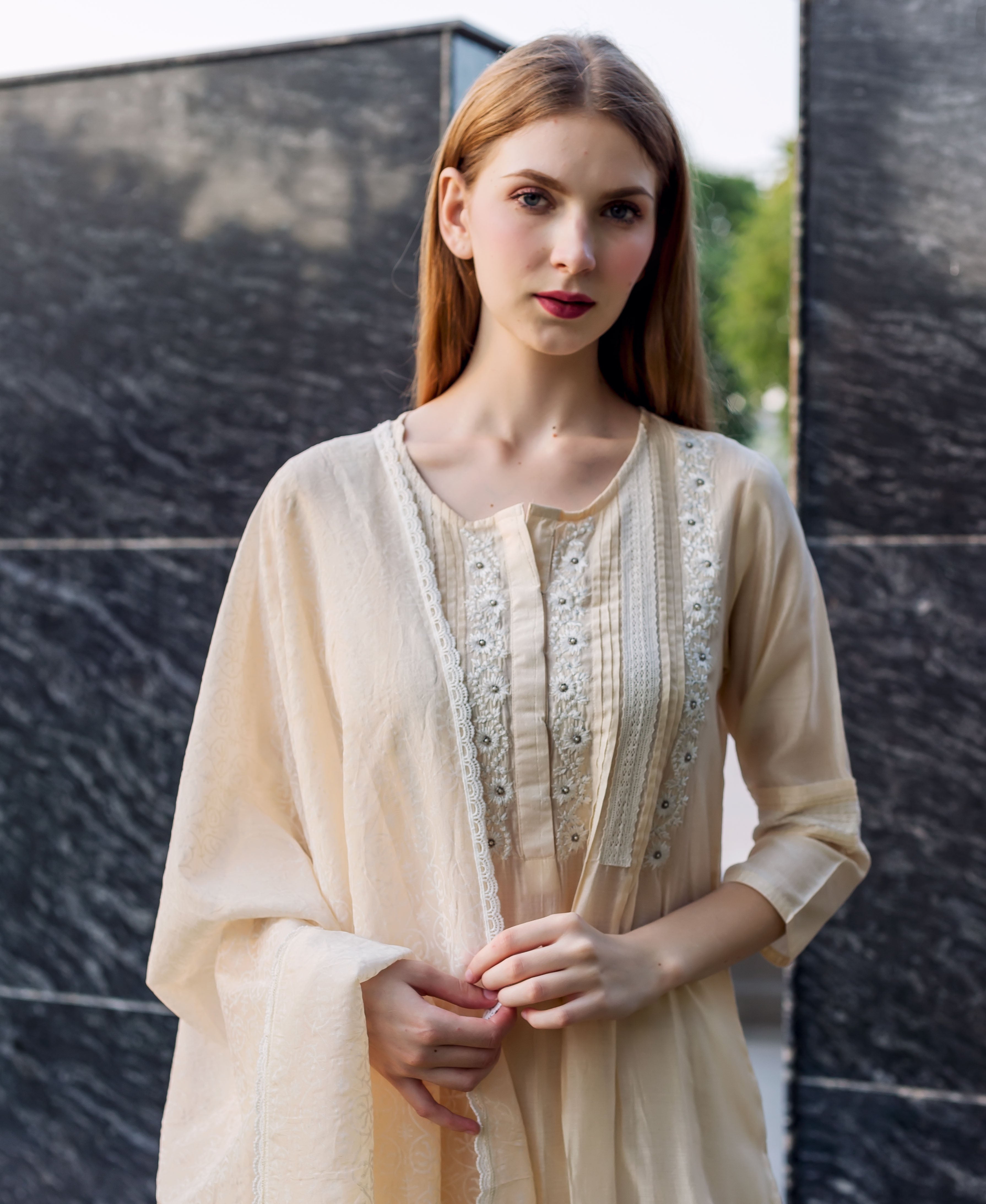 Front view of model wearing an off-white embroidered kurta with pintuck and lace details.