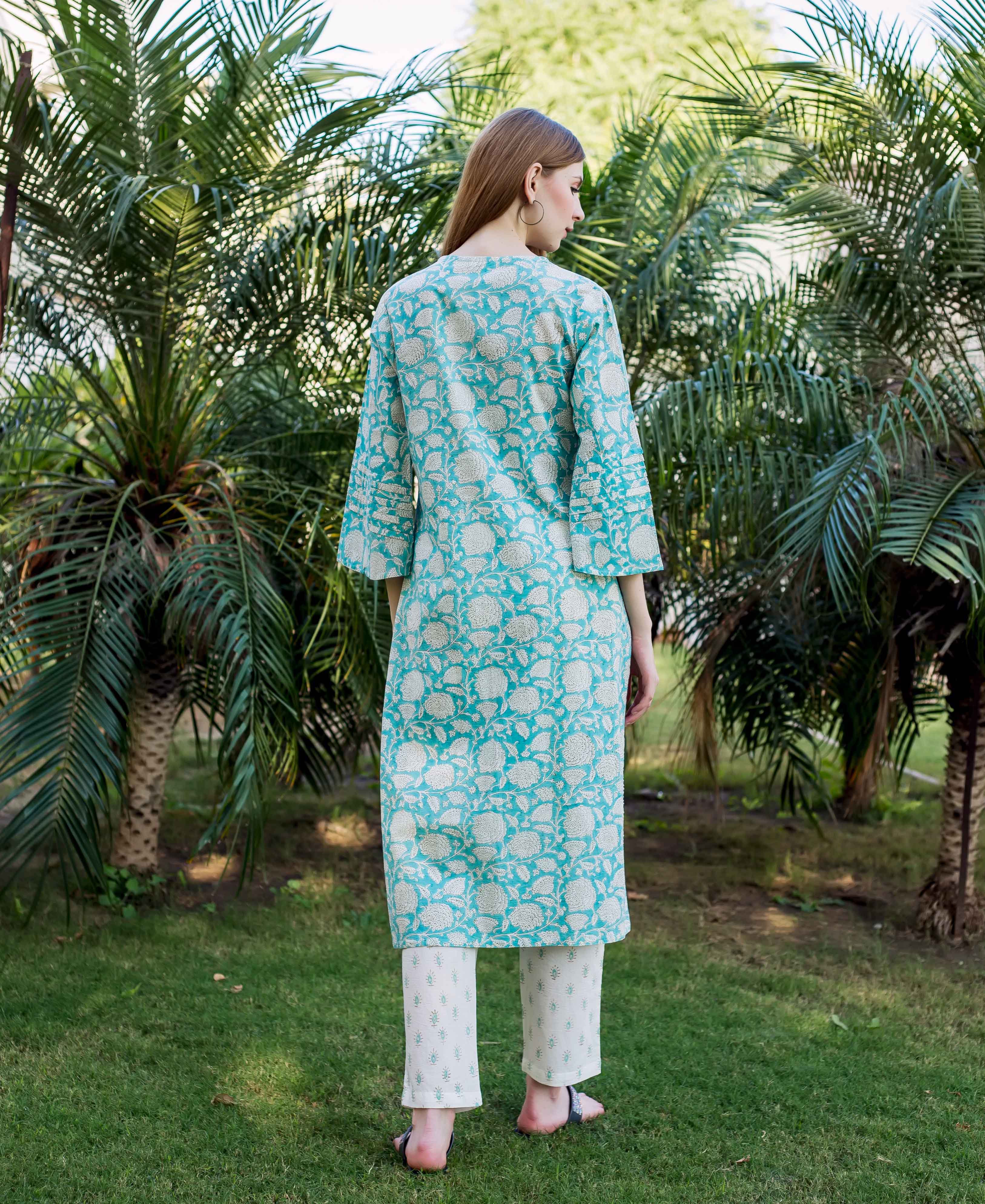 Teal kurta with white floral print, embroidered details, and white pants on a model outdoors.