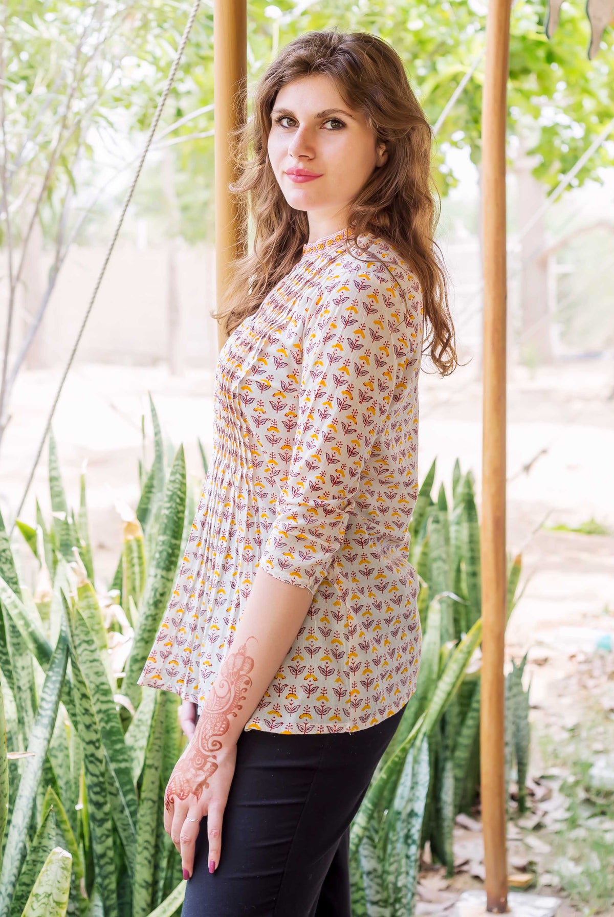 Side view of model wearing white block printed pintuck ethnic top with yellow and red print.
