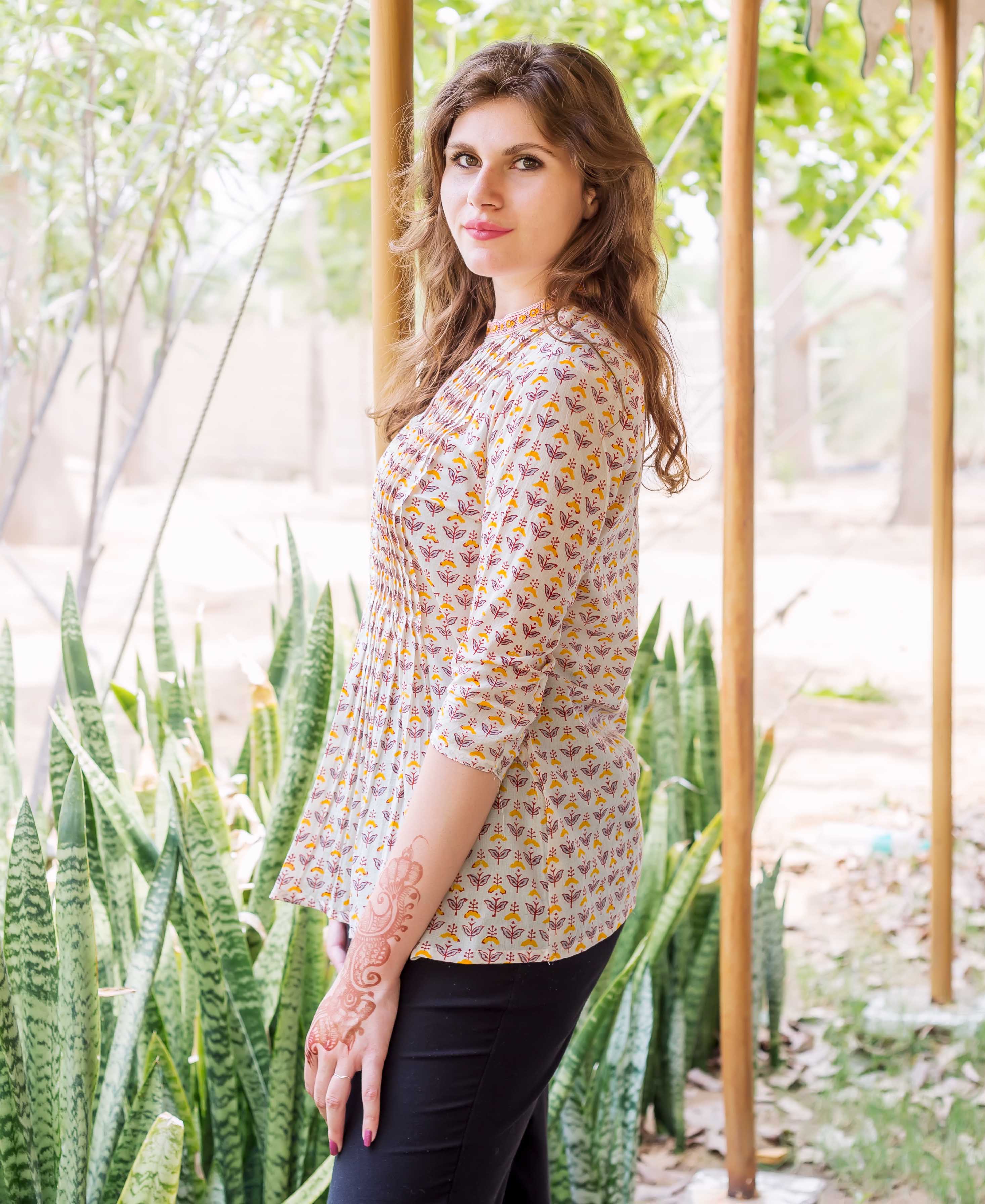 Side view of model wearing white block printed pintuck ethnic top with yellow and red print.