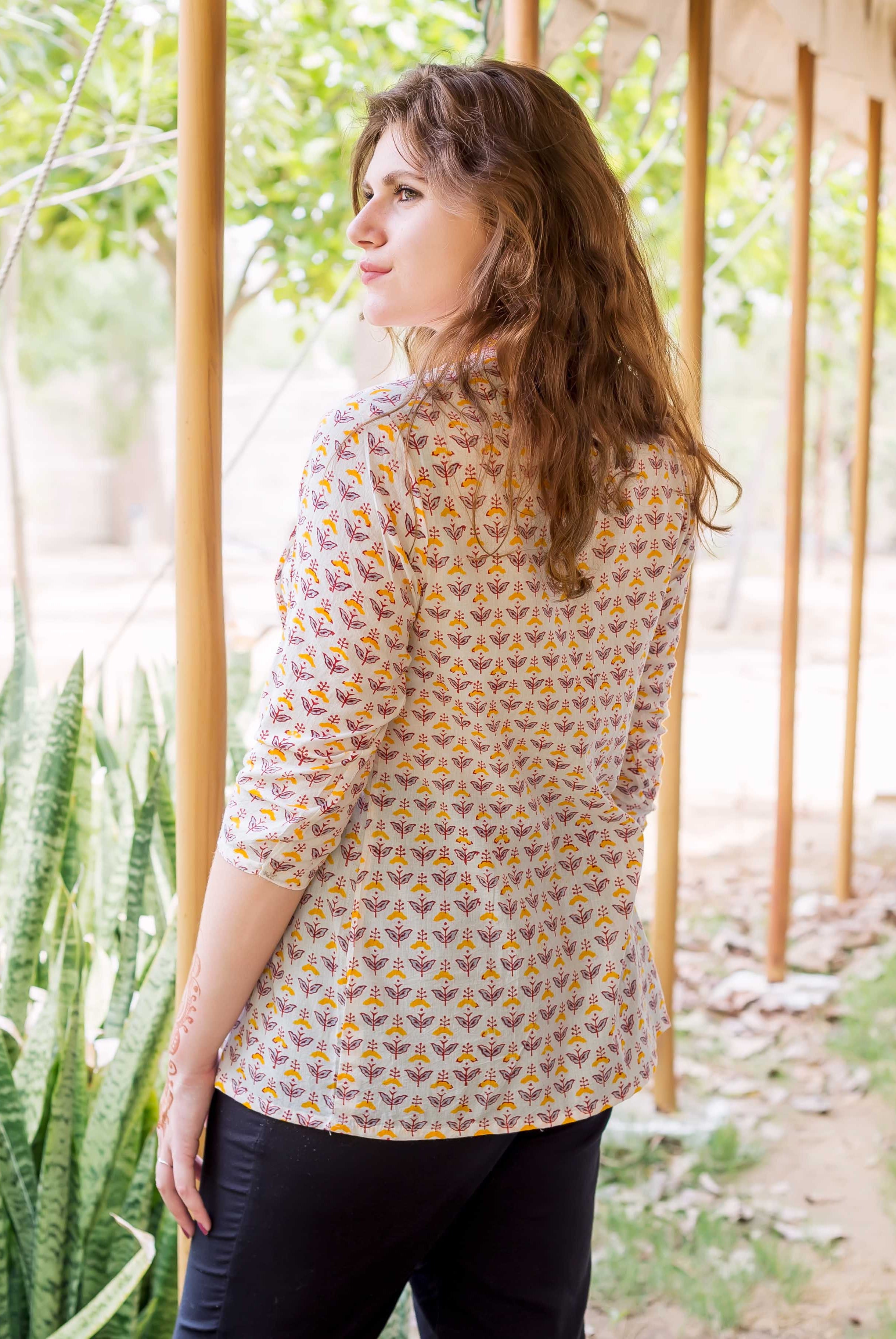 Model wearing white block-printed pintuck ethnic top, yellow and maroon floral pattern, looking left.