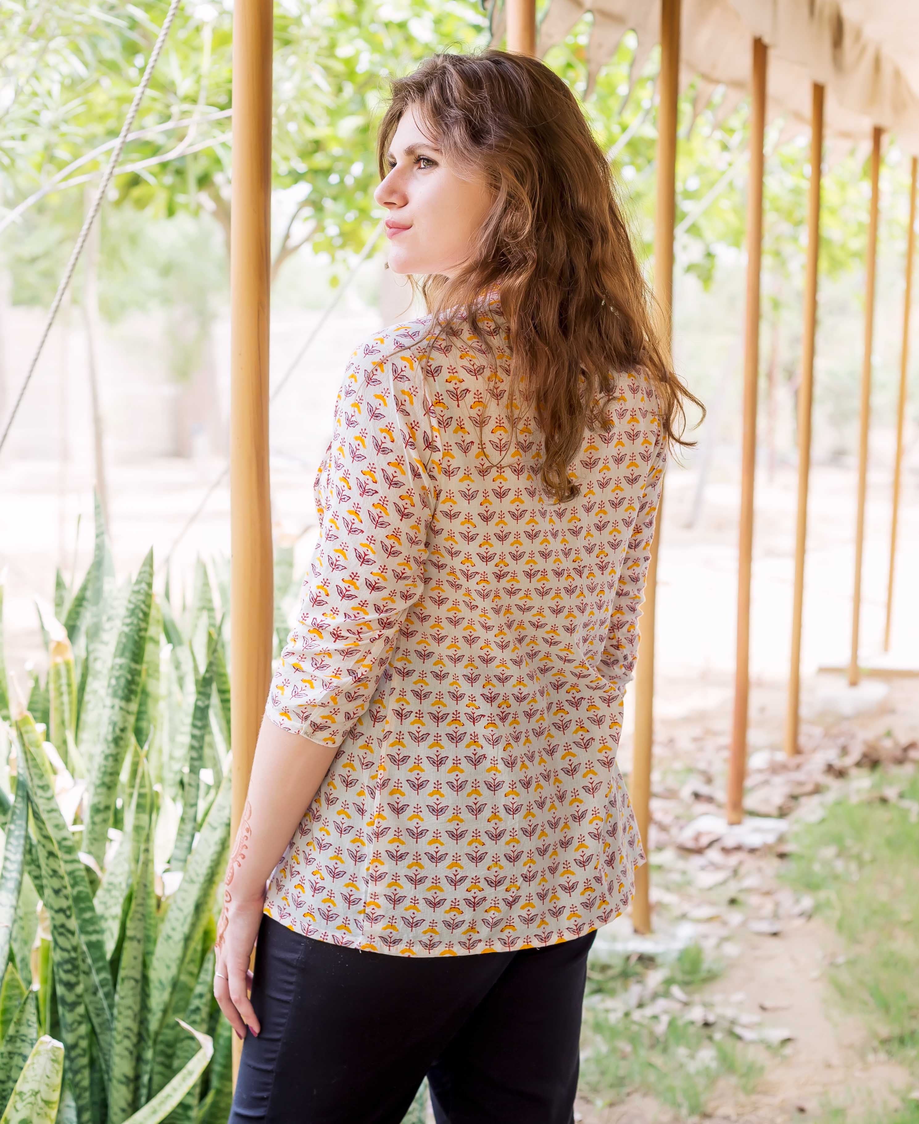 Model wearing white block-printed pintuck ethnic top, yellow and maroon floral pattern, looking left.