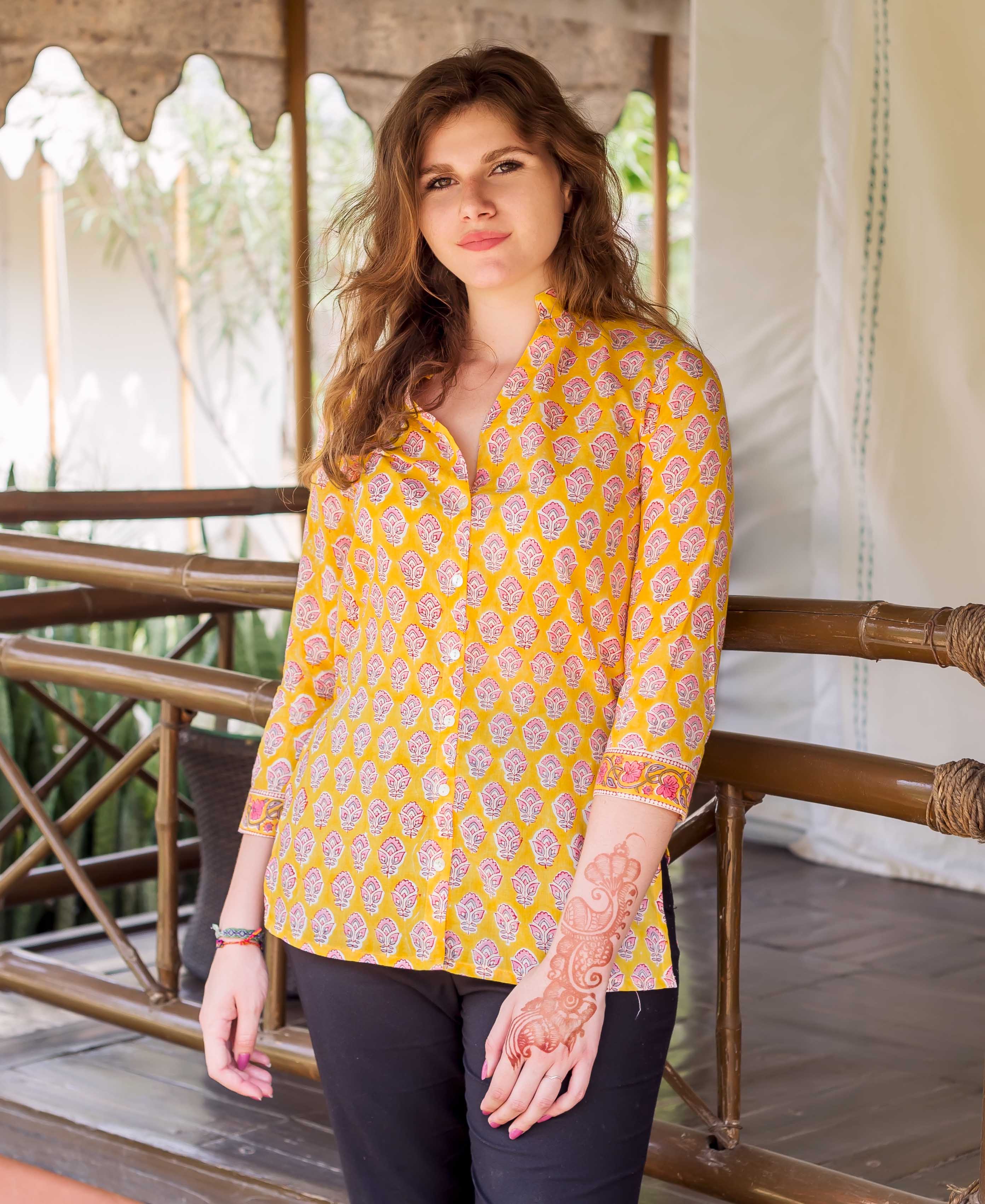 Woman wearing a yellow block-printed button-down shirt with pink paisley motifs, front view.