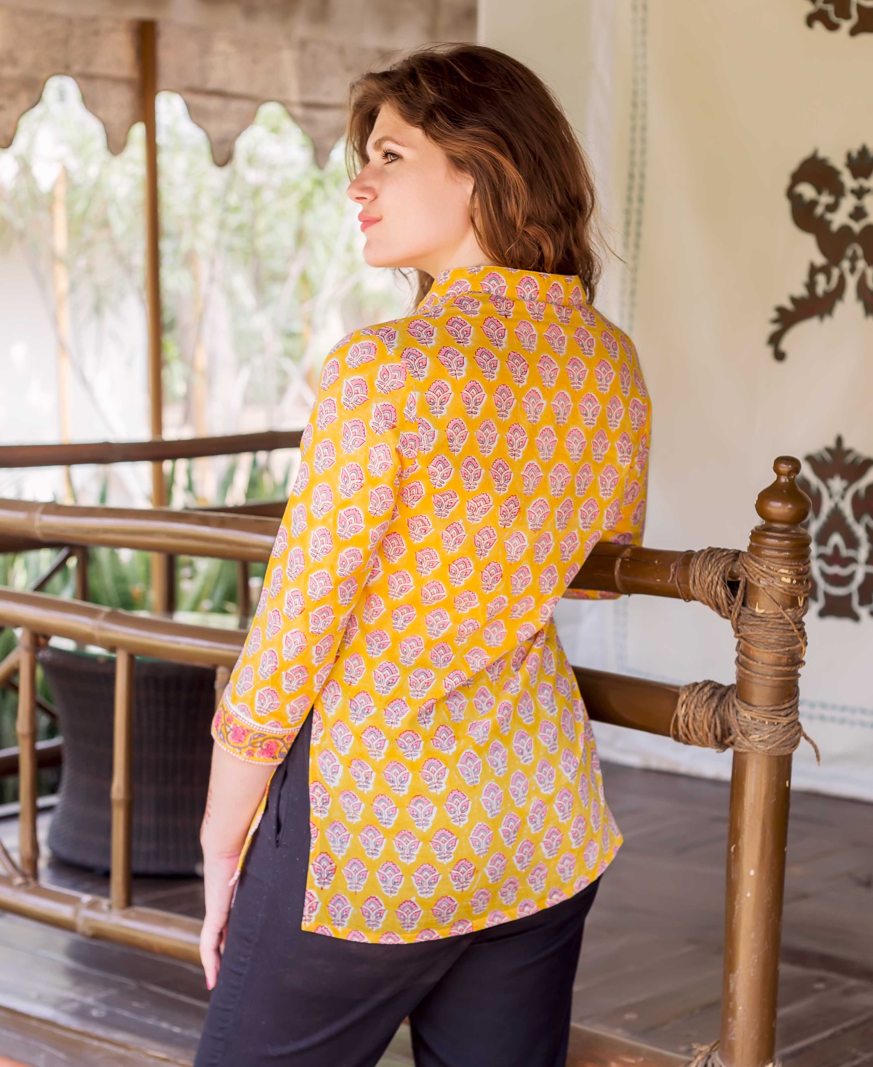 Model wearing yellow hand-block-printed shirt with pink ethnic floral patterns, back view.
