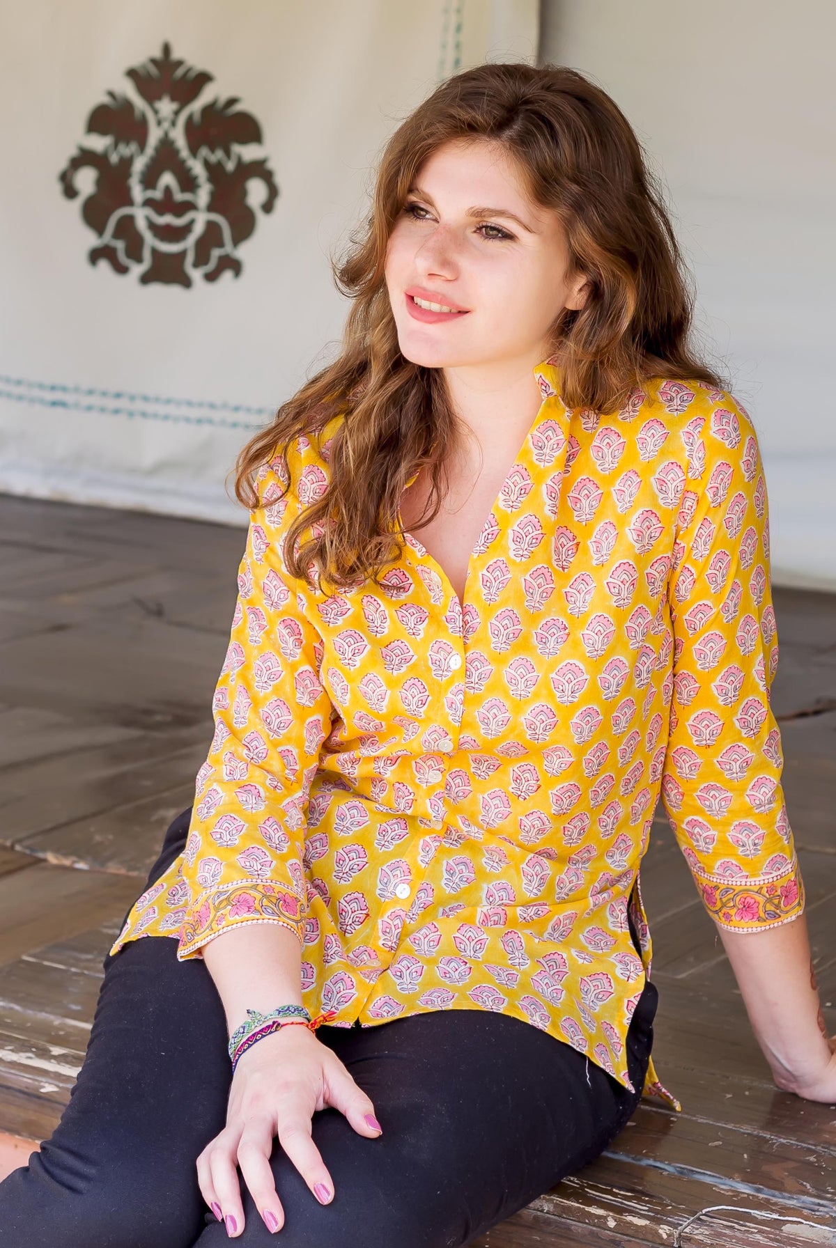 Seated model in a yellow button-down shirt with pink and coral block print.