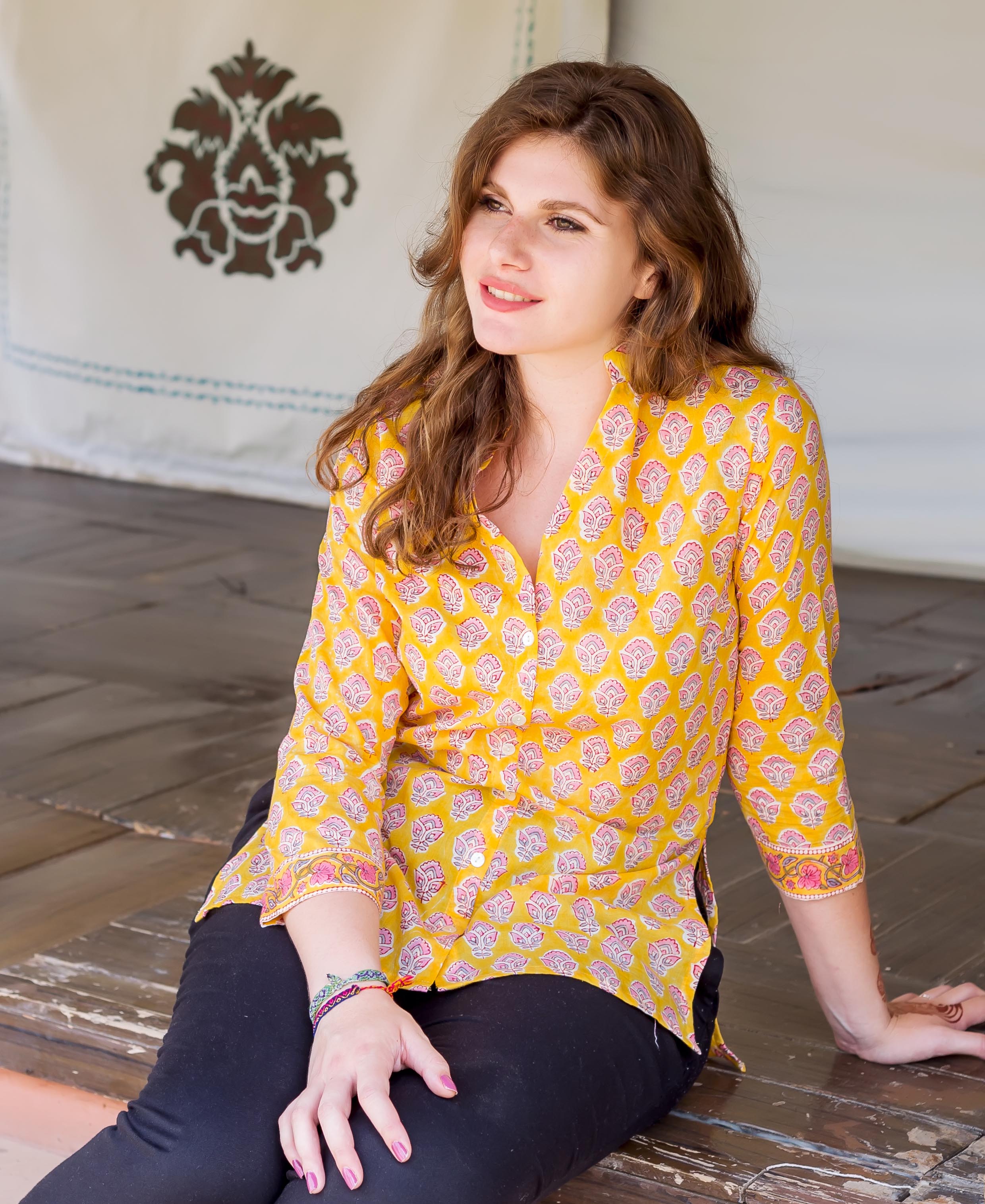 Seated model in a yellow button-down shirt with pink and coral block print.
