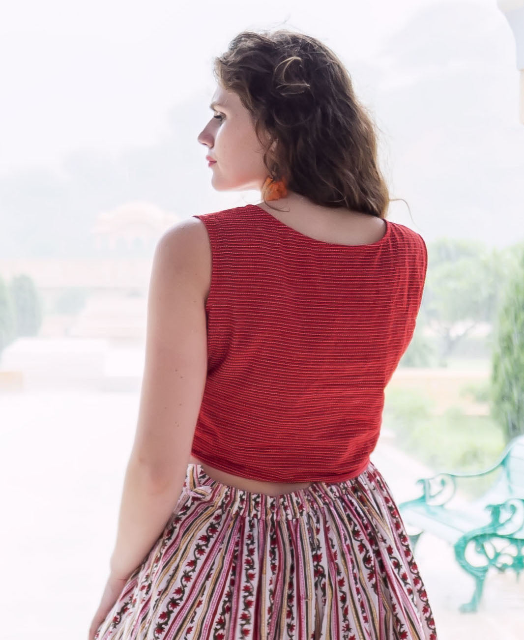 Model wearing a red yarn-dyed crop top with a colorful striped floral skirt, seen from behind.