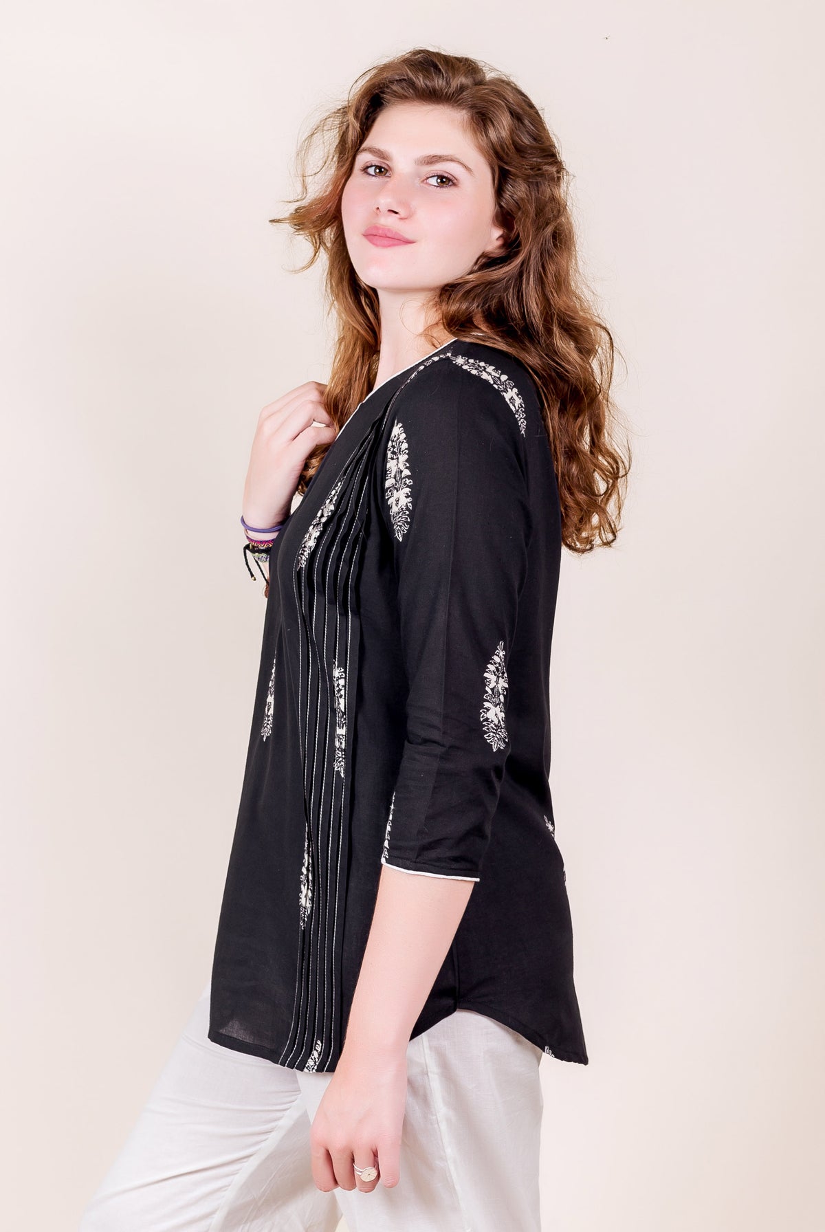 Angled view of model in black hand-block printed cotton top with white designs.