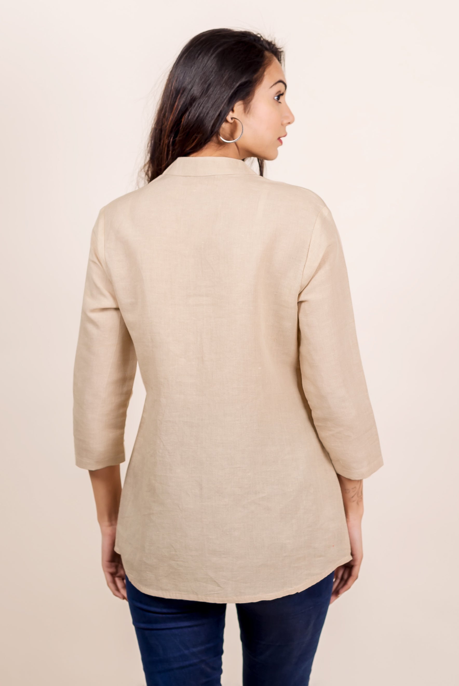 Rear view of model wearing a plain beige linen top with a mandarin collar.
