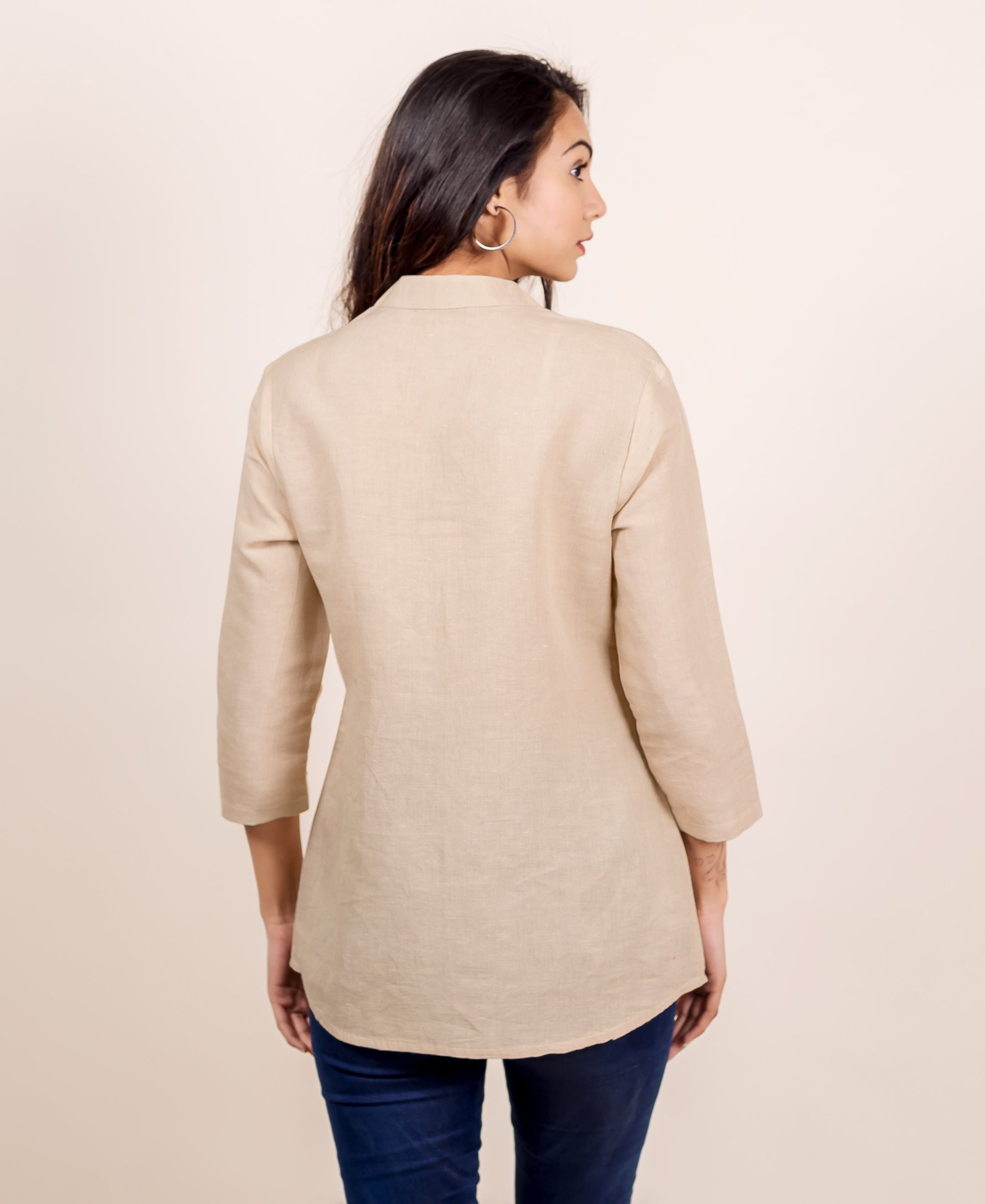 Rear view of model wearing a plain beige linen top with a mandarin collar.