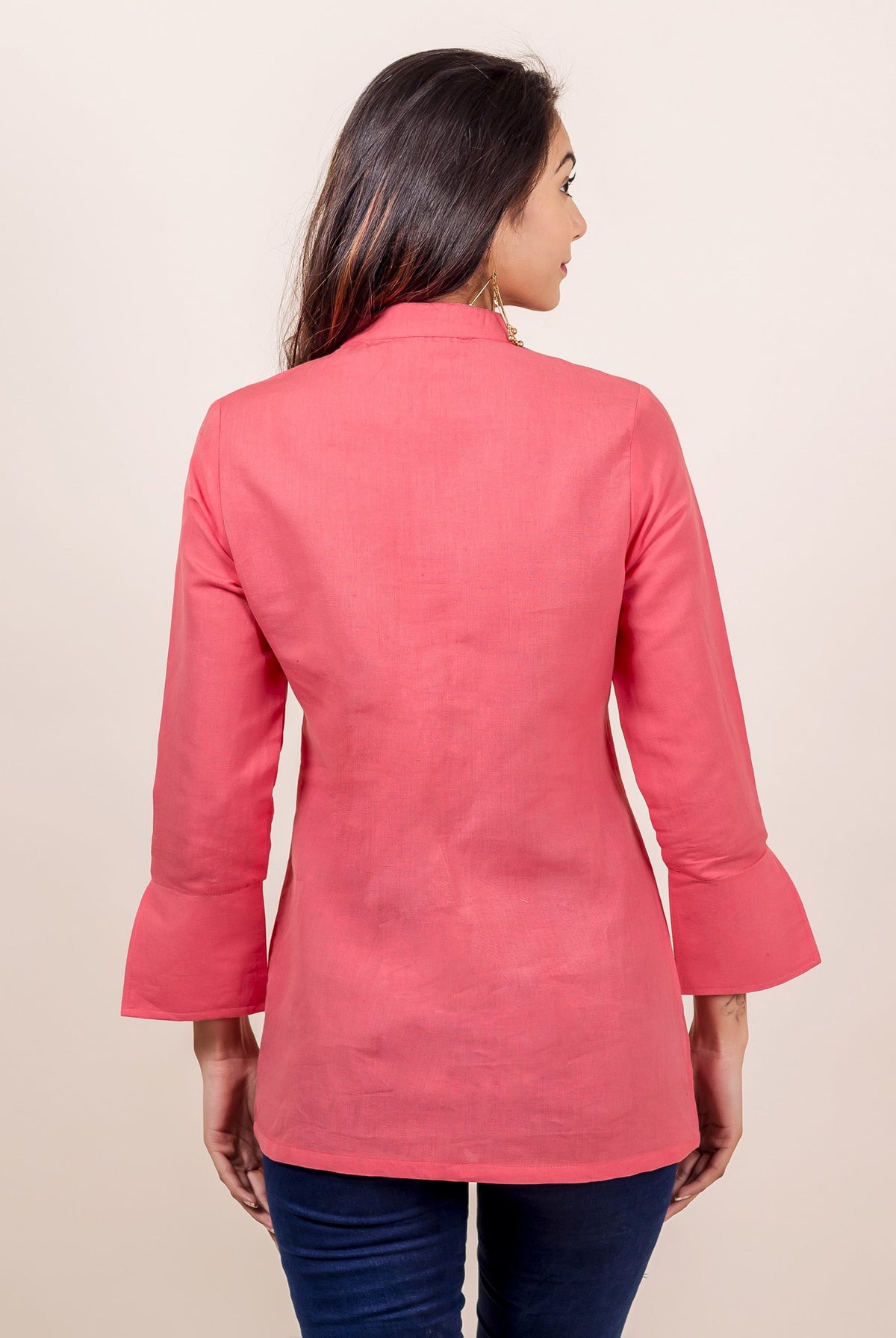 Rear view of a model in a peach linen top with high collar and bell sleeves.