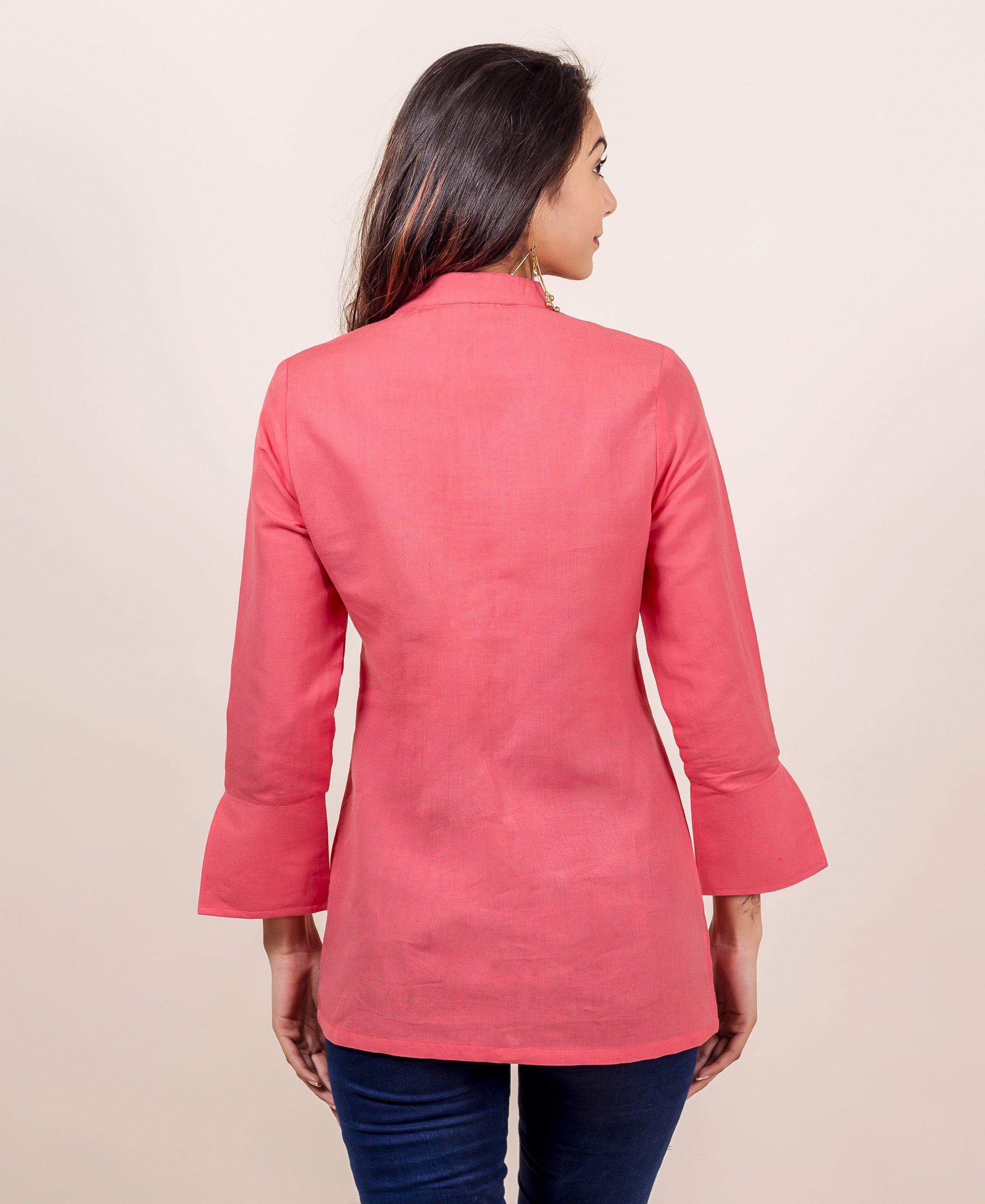Rear view of a model in a peach linen top with high collar and bell sleeves.