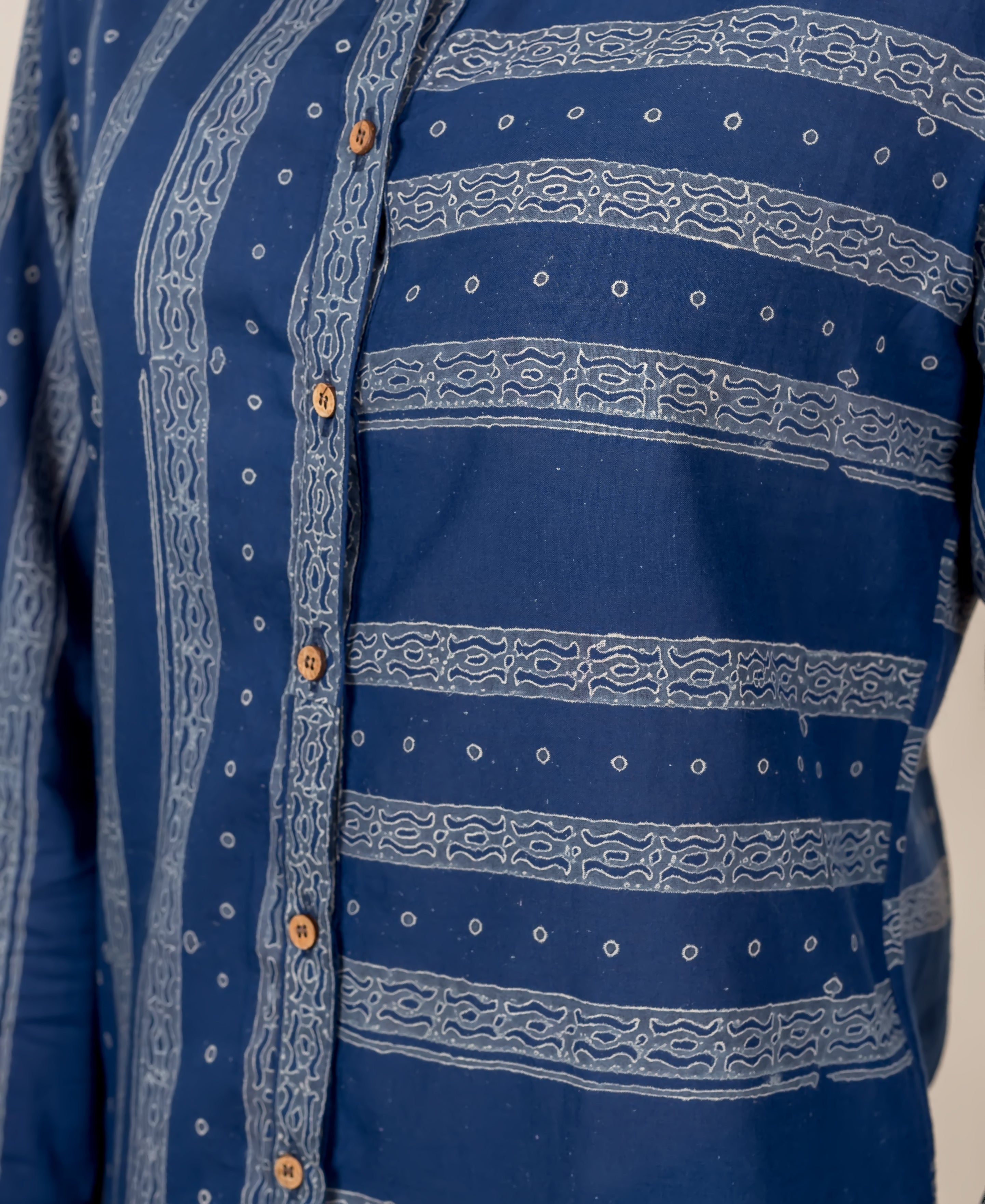 A close-up of a blue, block-printed button-down shirt with white designs.