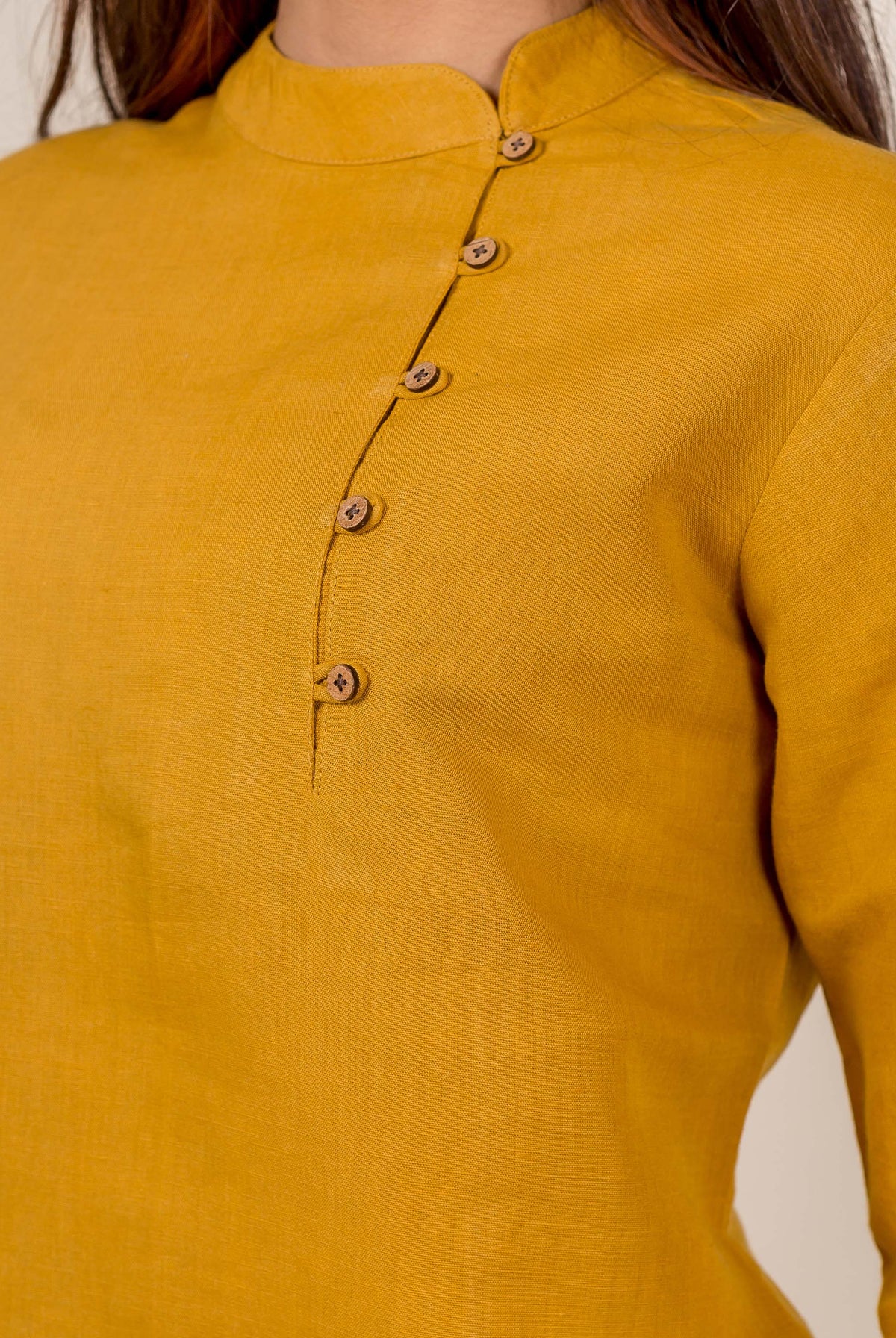 Close-up of a model wearing a mustard linen top with a mandarin collar and off-center buttons.