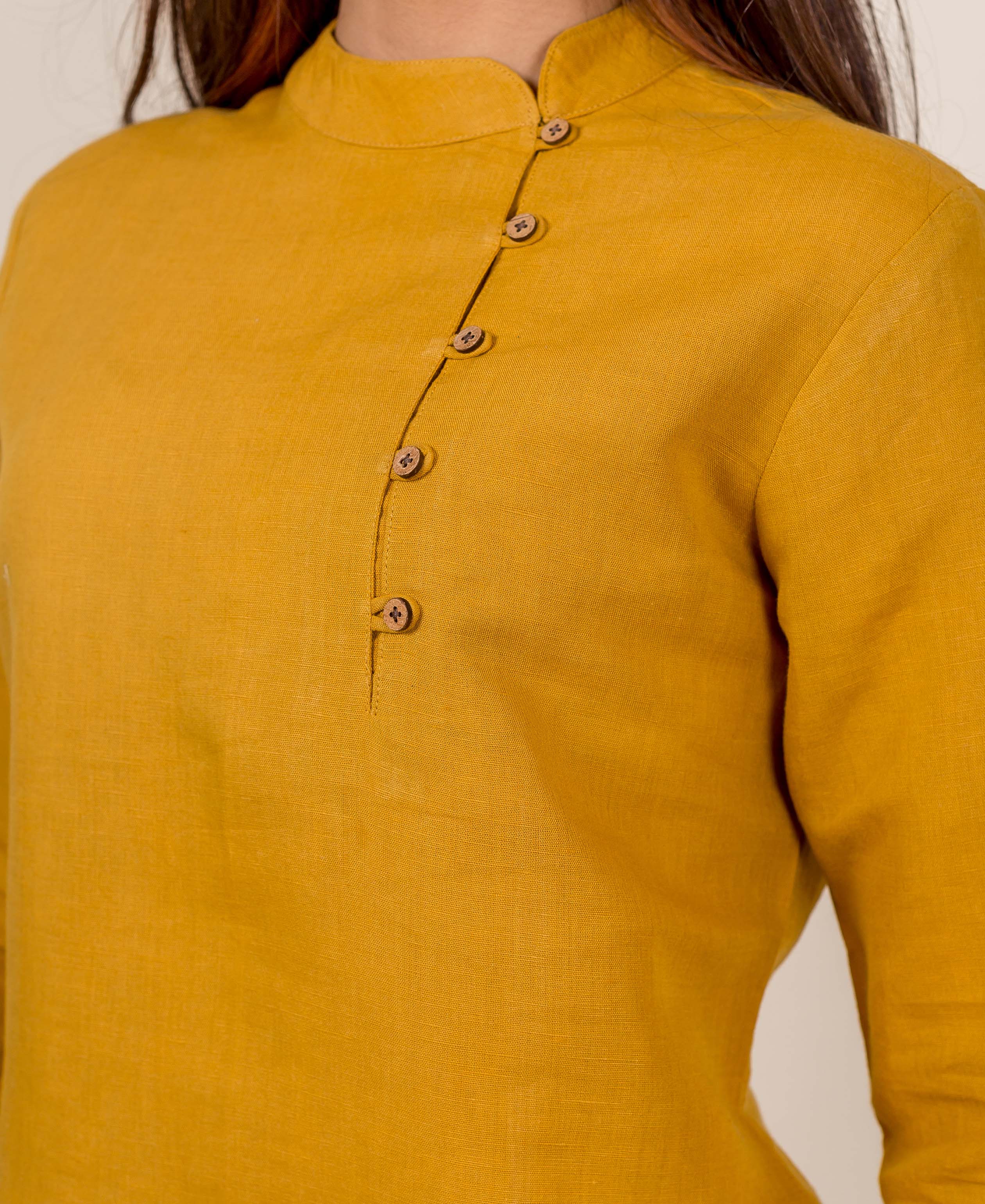 Close-up of a model wearing a mustard linen top with a mandarin collar and off-center buttons.