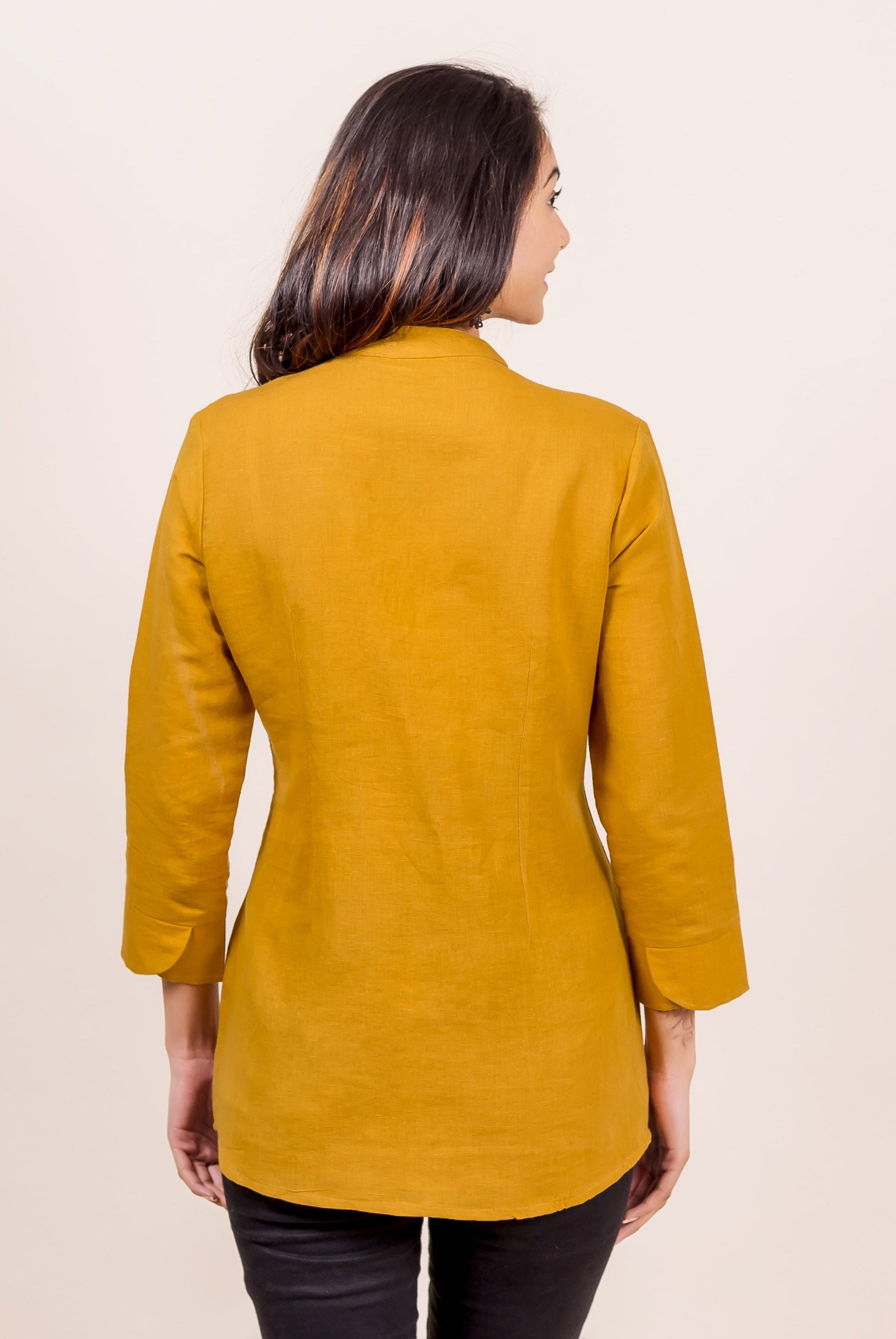 A model wearing a mustard linen mandarin collar top with a subtle block print.