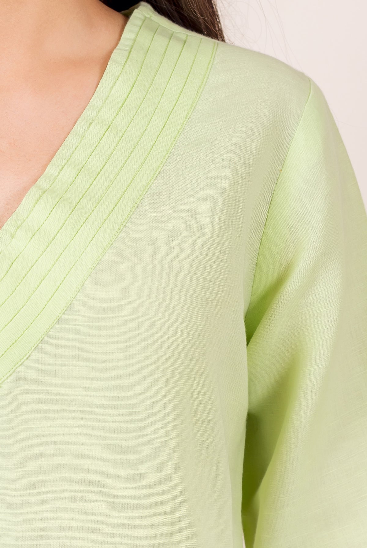Close-up of lime green linen top on model, V-neck featuring fine pintuck pleats.
