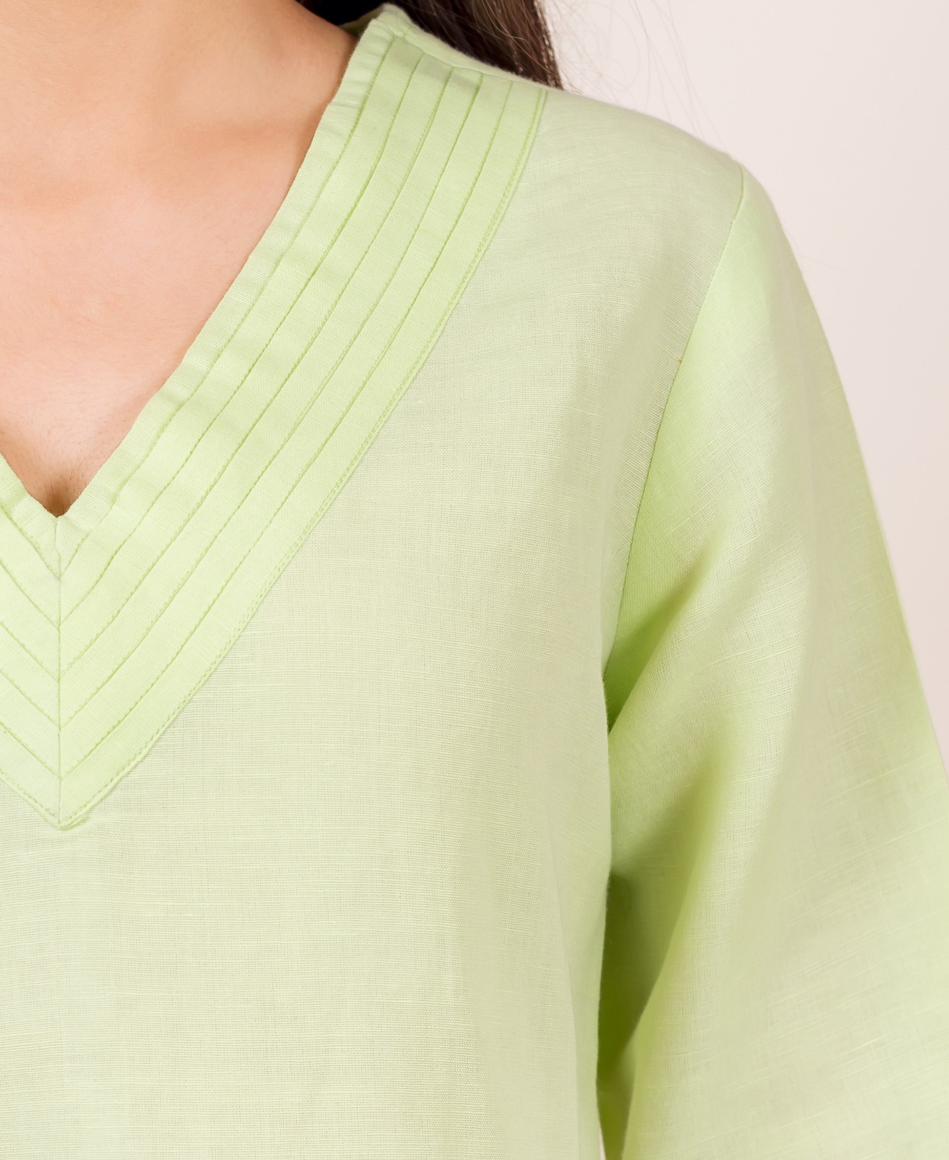 Close-up of lime green linen top on model, V-neck featuring fine pintuck pleats.
